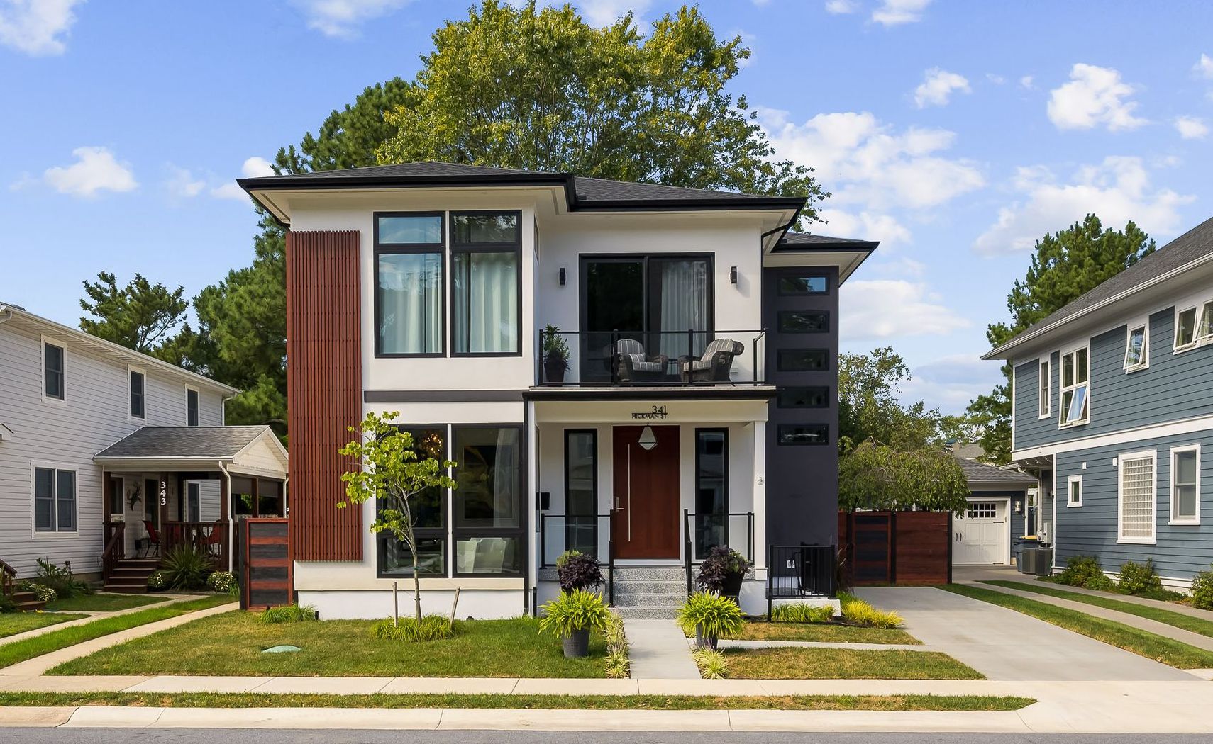 Modern two-story house with red door, black trim, and wood accents; surrounded by green lawn and other houses.
