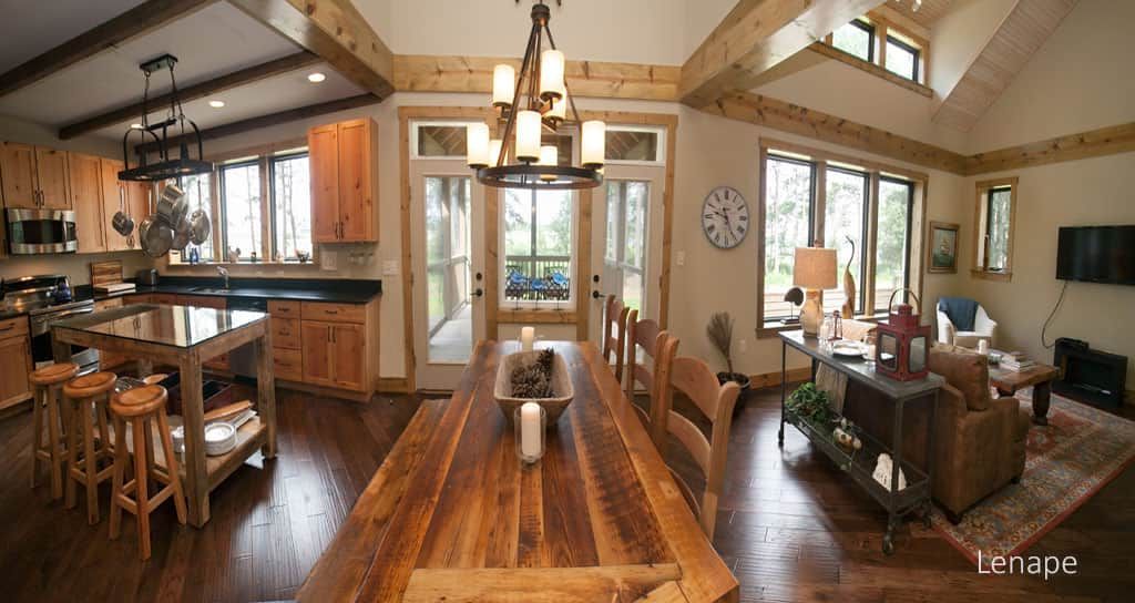 Spacious open-plan dining and living area with wood beams, kitchen with island, and large windows.