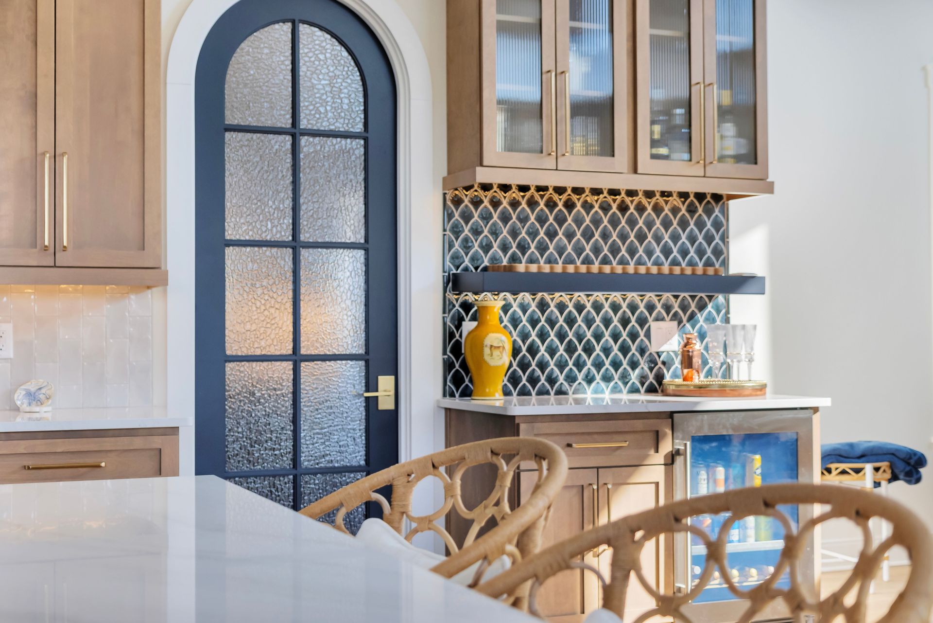 Kitchen with arched dark blue door, beaded tile backsplash, and wooden cabinets.