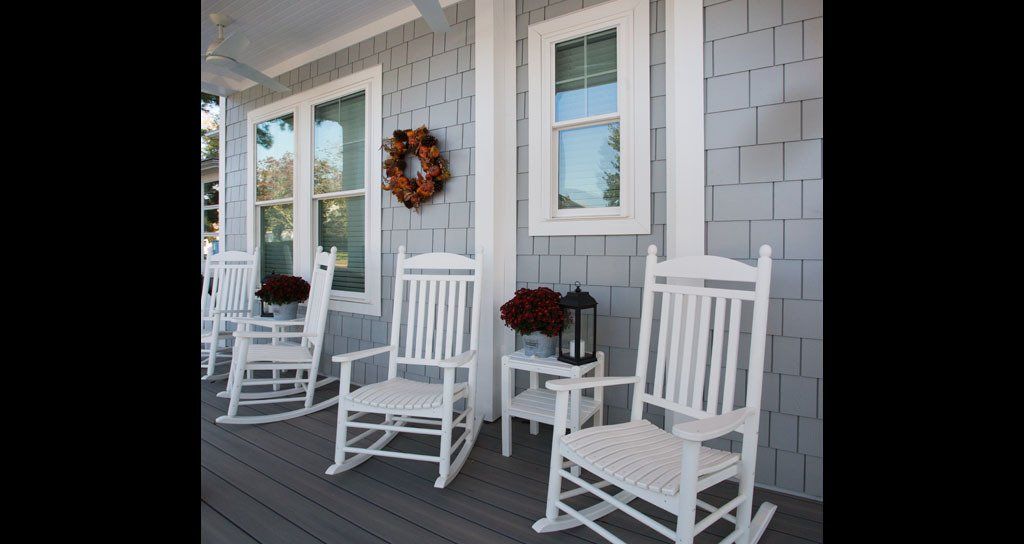 White rocking chairs on a front porch with gray siding and fall wreath.