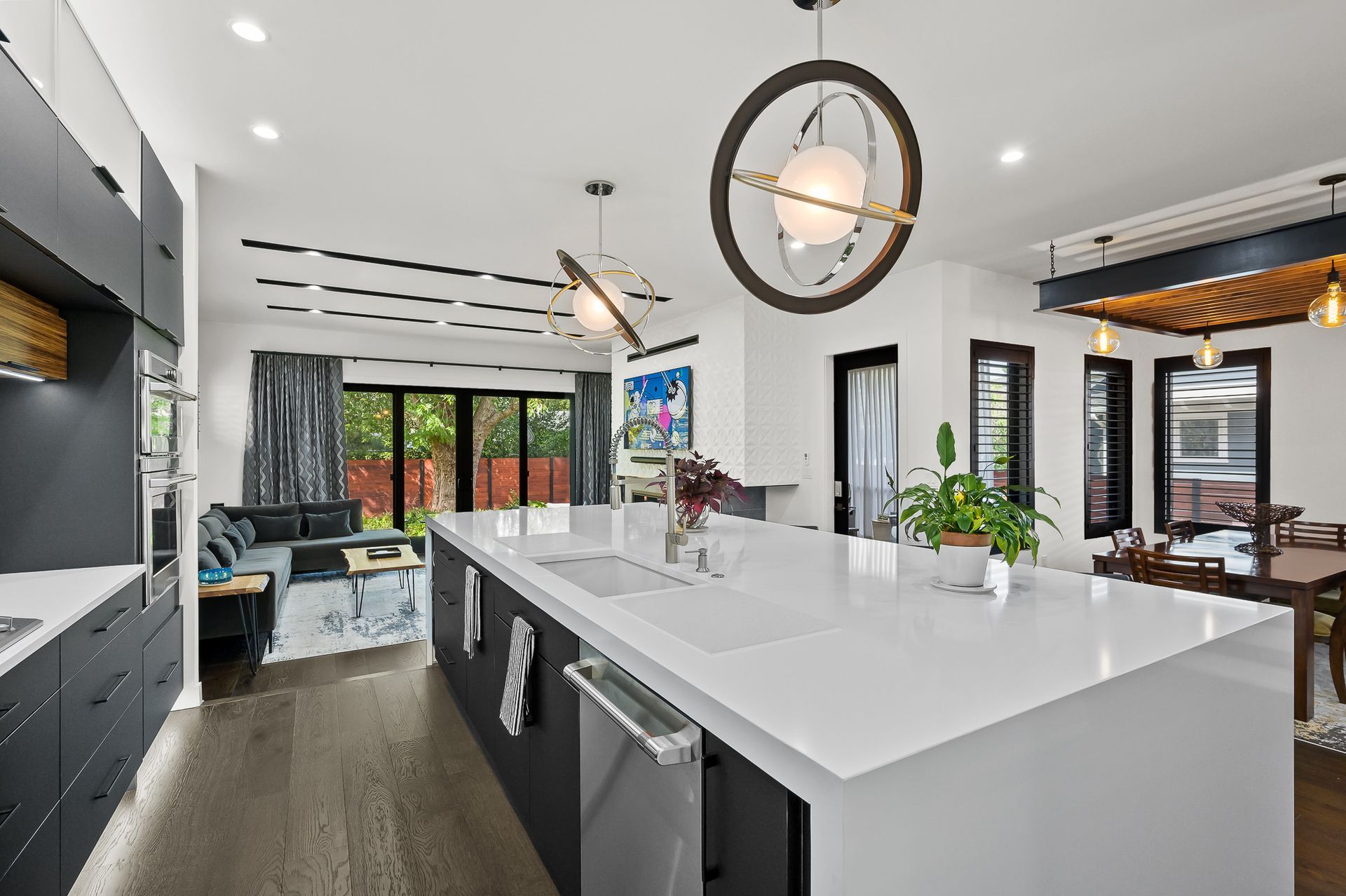 Modern kitchen with large white island, dark cabinets, pendant lights, and open to a dining area.