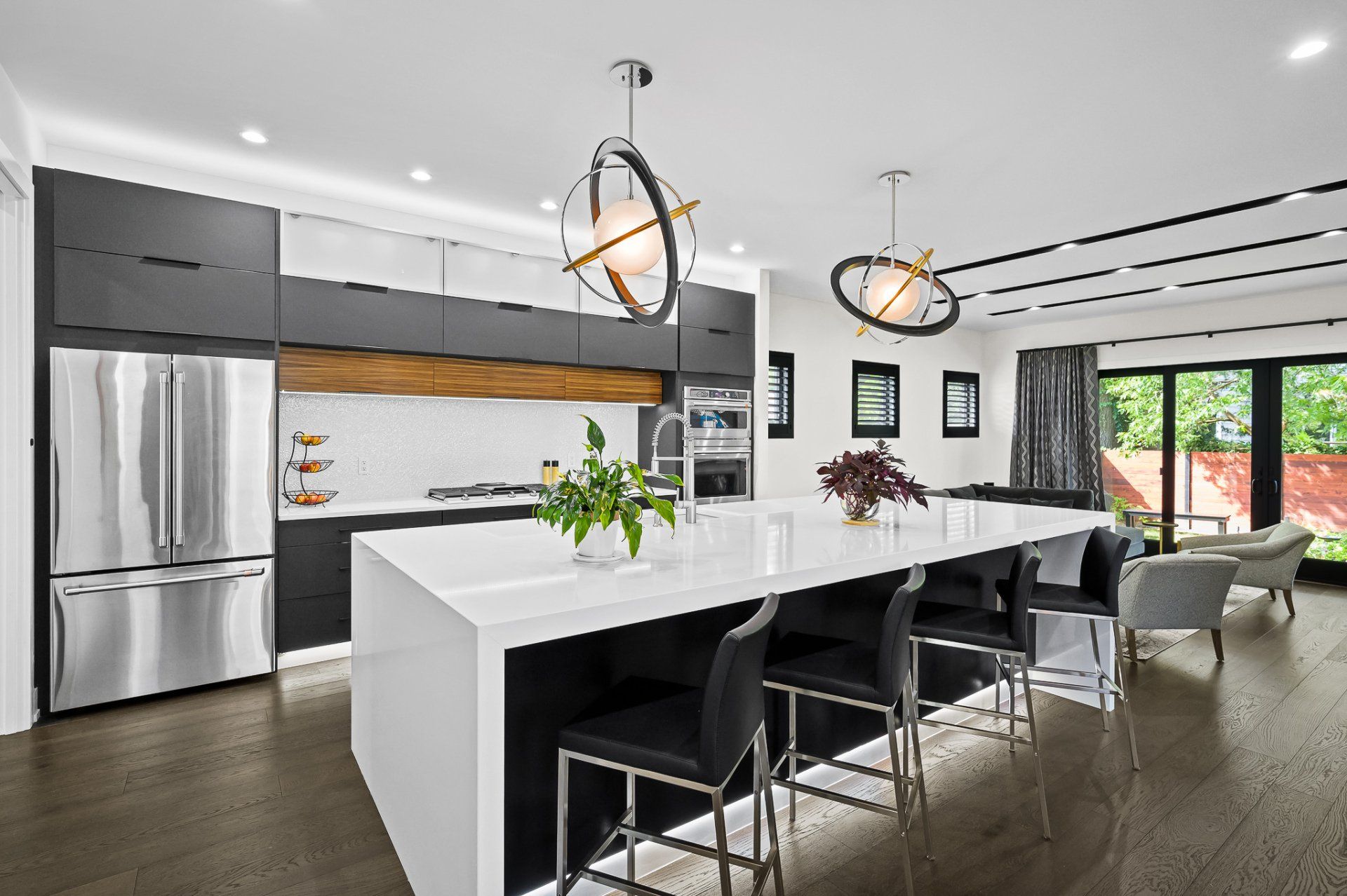 Modern kitchen with large white island, dark cabinets, stainless steel appliances, and pendant lights.