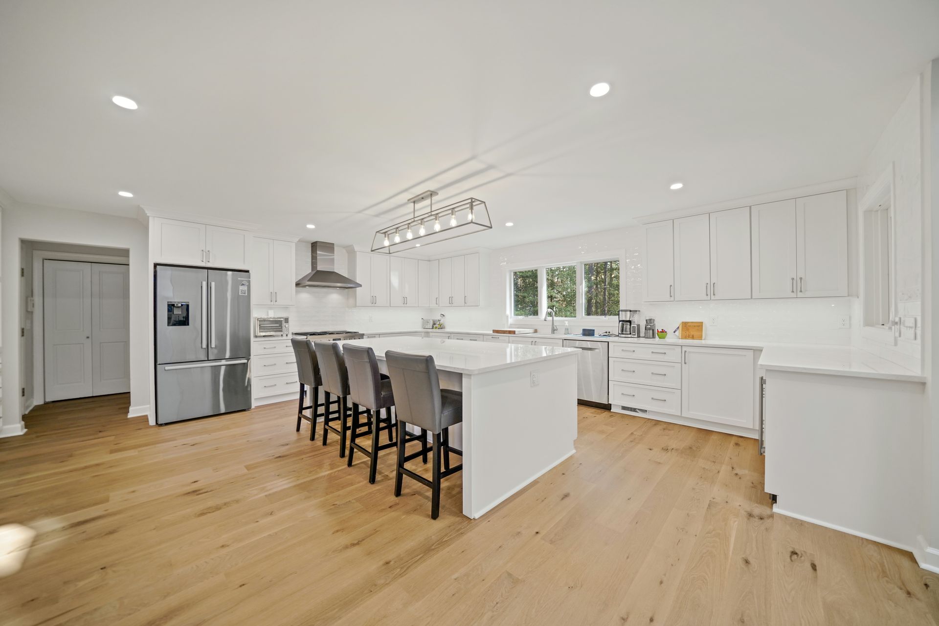 Bright white kitchen with wood floors, large island with seating, stainless steel appliances.