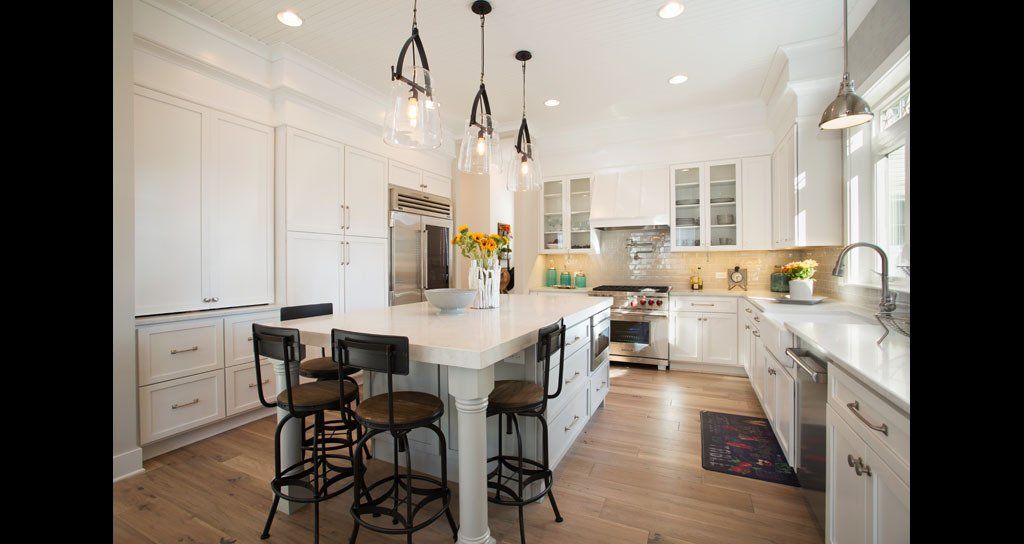 Bright, white kitchen with a large island, stainless steel appliances, and hanging lights.