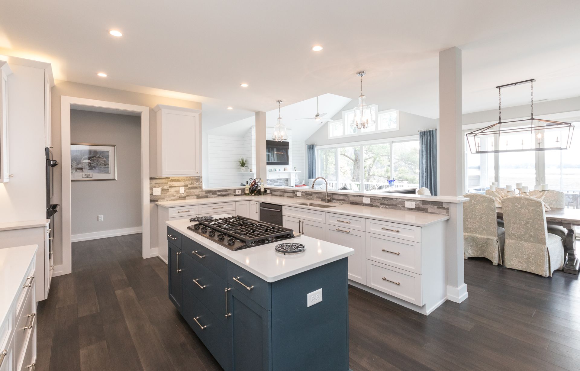 Modern kitchen with island and gas cooktop. White and blue cabinets, wood floors.