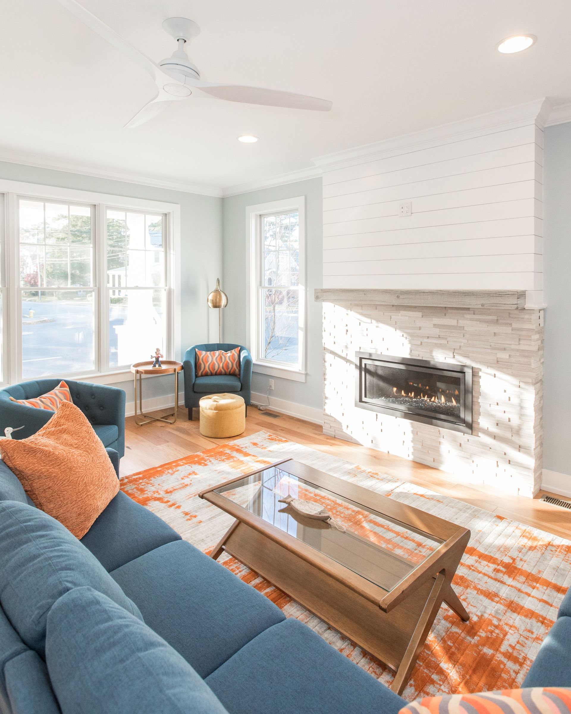 Living room with blue sofa, orange rug, white brick fireplace, and large windows.