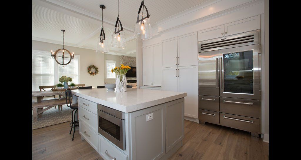 Modern kitchen with island and stainless steel refrigerator. Light wood floors, white cabinets, pendant lights.
