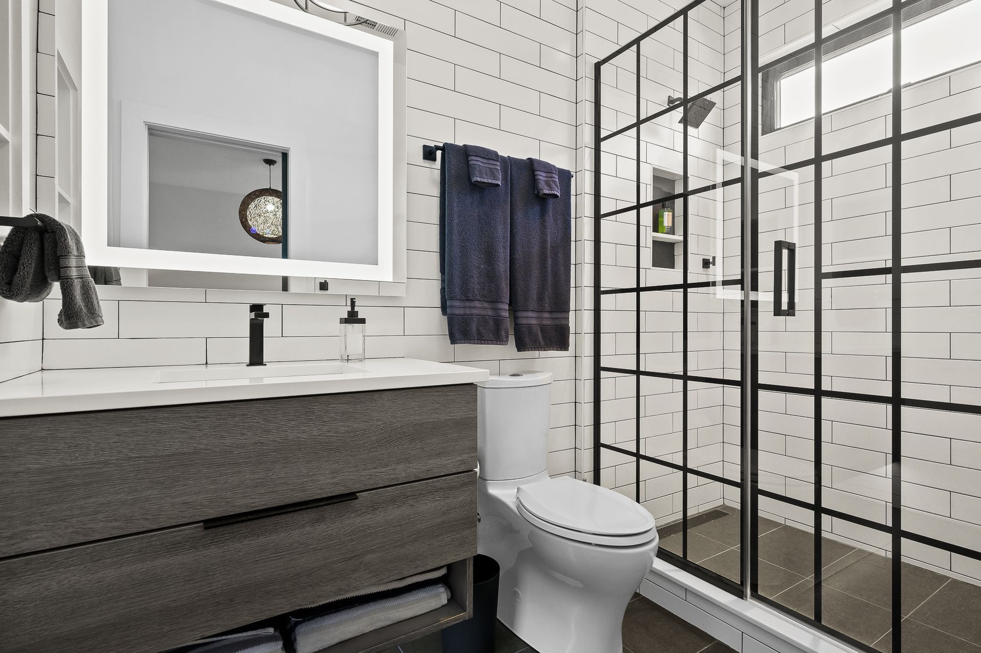 Modern bathroom with a gray vanity, white subway tile, and a black-framed shower.