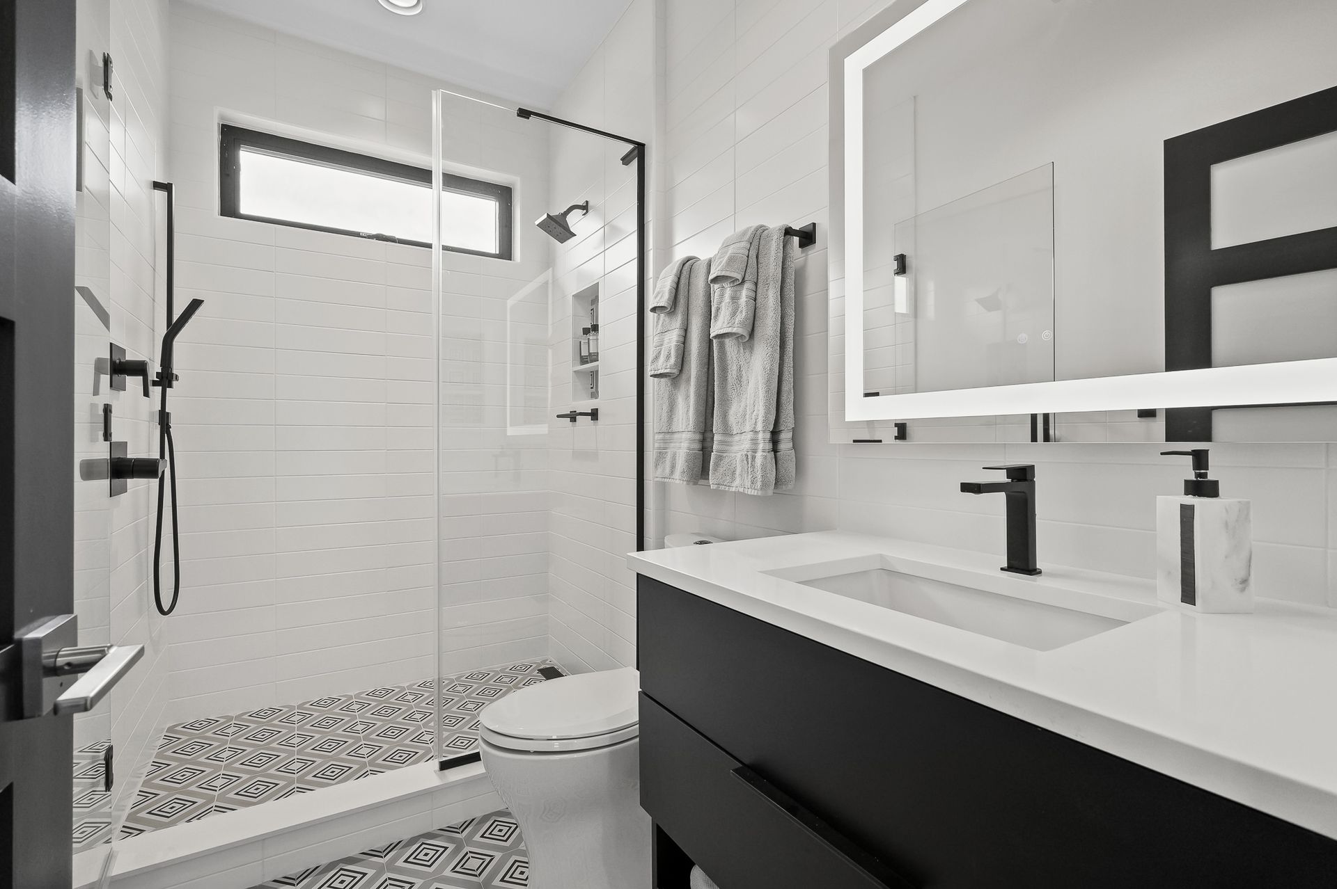 Modern black and white bathroom. Shower with glass door, vanity with sink, and mirror with light.