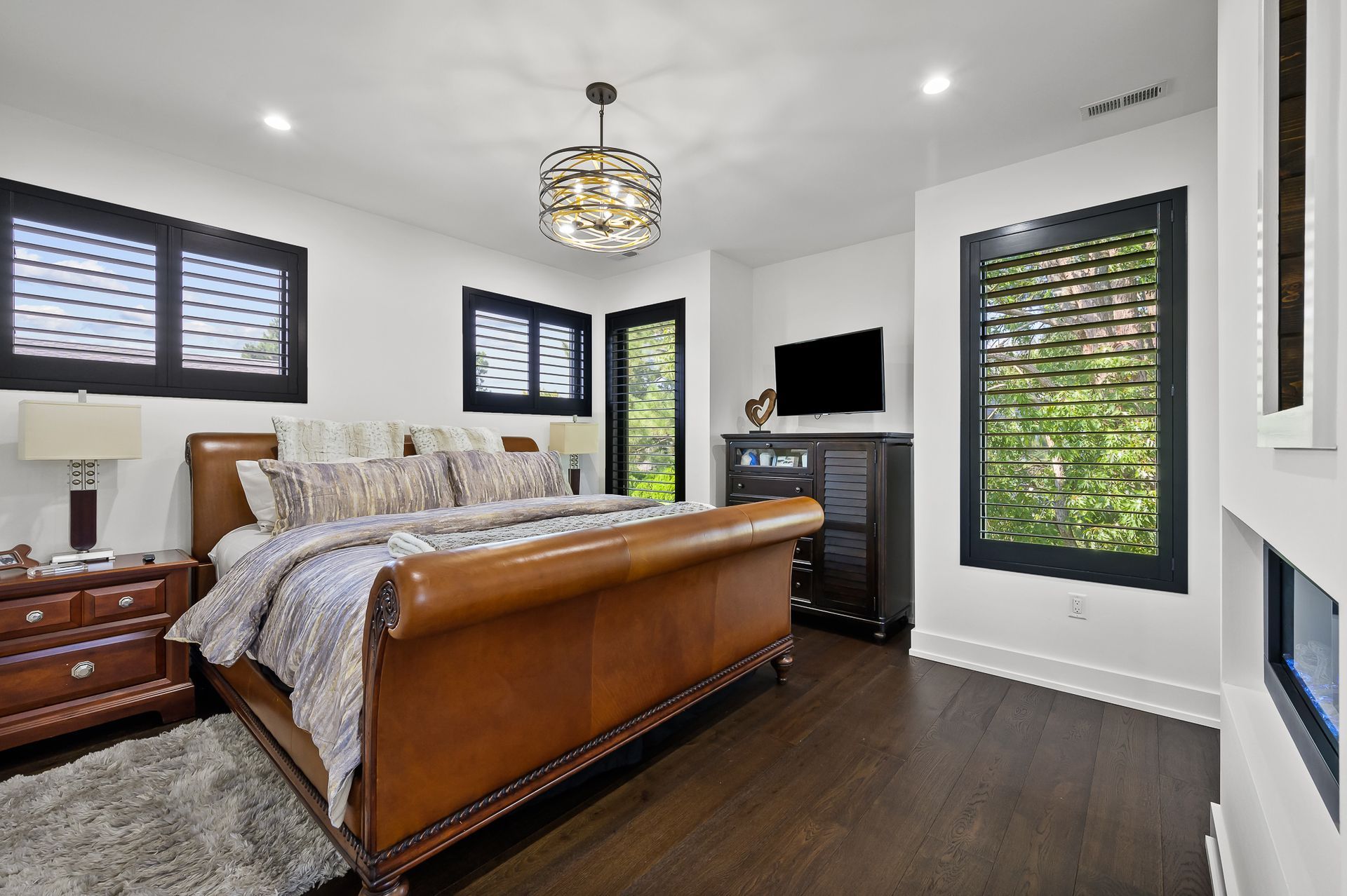 Bedroom with leather bed, dark wood floor, and black shutters on windows.