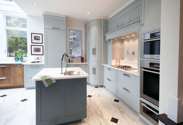 Elegant light blue kitchen with marble floors, island, and built-in appliances.