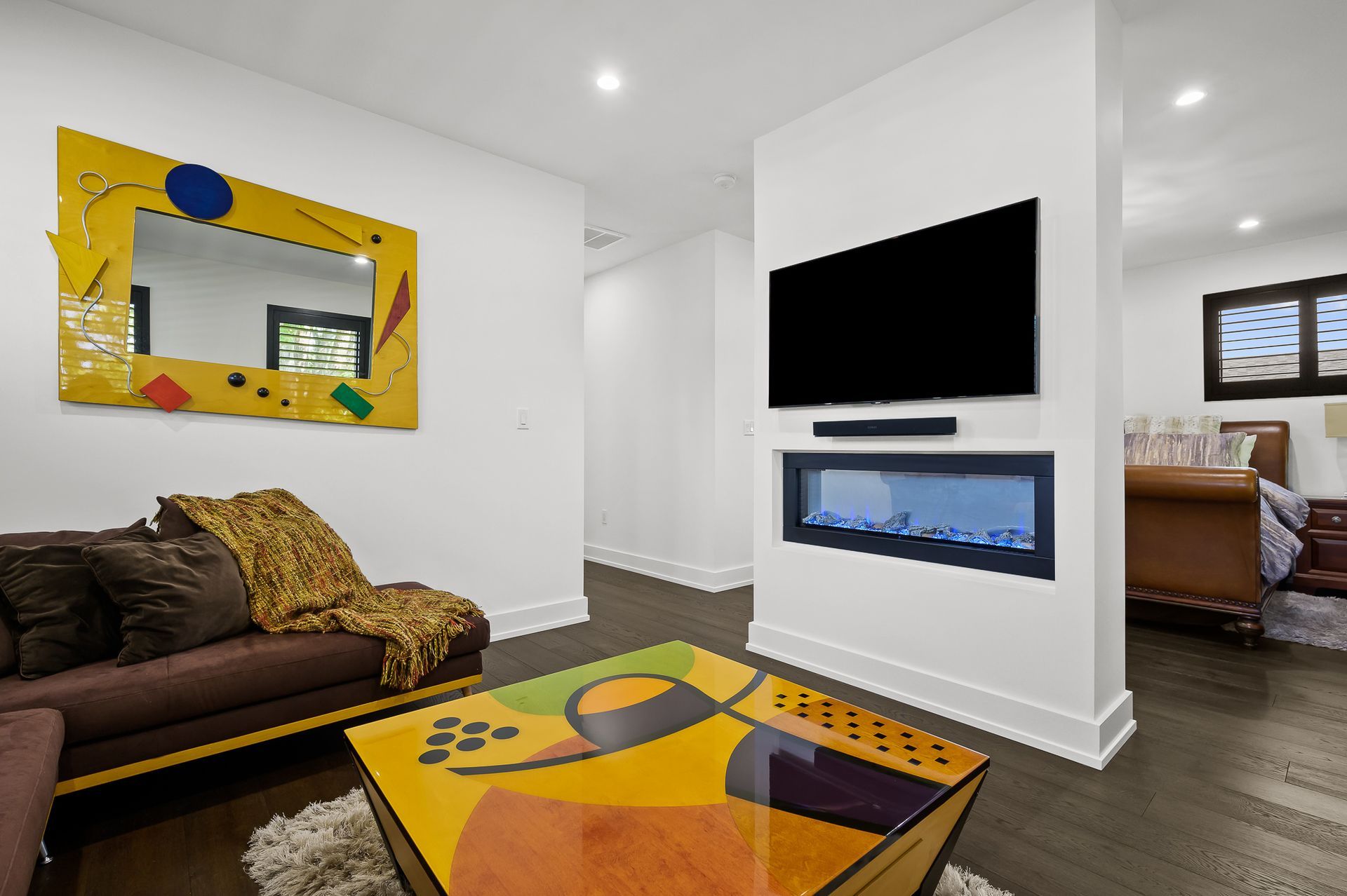 Living room with sofa, coffee table, fireplace, TV, and mirror. Modern decor, dark wood floors.