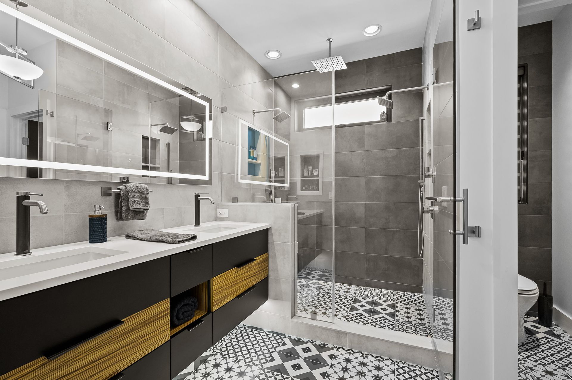 Modern bathroom with gray tiled walls, glass shower, and patterned floor.