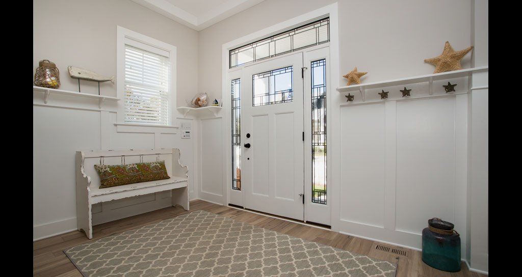 White coastal-style entryway with light wood floor, bench, rug, door, and wall decor.