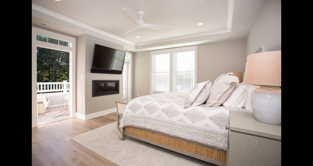 Bedroom with bed, fireplace, TV, and access to a balcony; neutral colors.