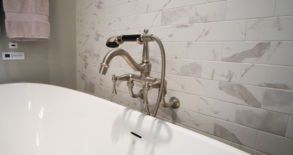 Bathroom with white tub, silver faucet, and marble tile wall. Pink towel hangs on the left.