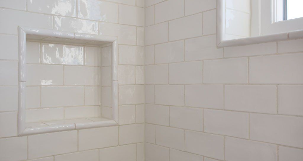 White tiled shower with built-in shelf and window, suggesting a clean bathroom.