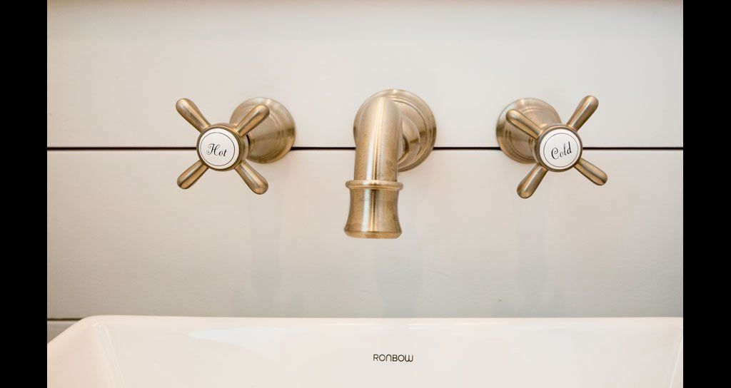 Gold faucet with cross-shaped handles above a white sink, set against a white tiled wall.