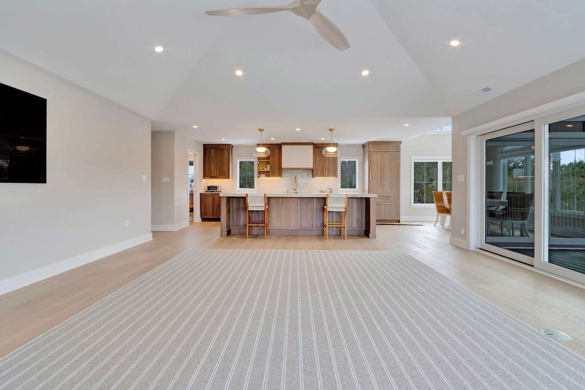 Open-plan kitchen and living area with light wood floors, a large rug, and sliding glass doors.