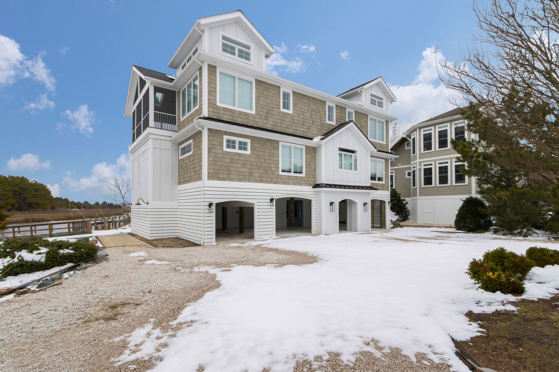 Multi-story beach house on a snowy day, with white trim and gray siding. Open carport beneath.