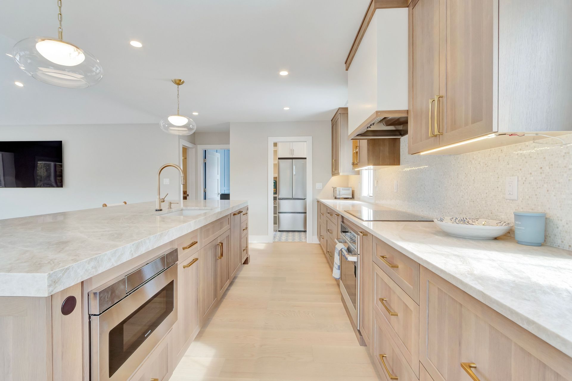 Modern kitchen with light wood cabinets, marble countertops, stainless steel appliances, and two pendant lights.