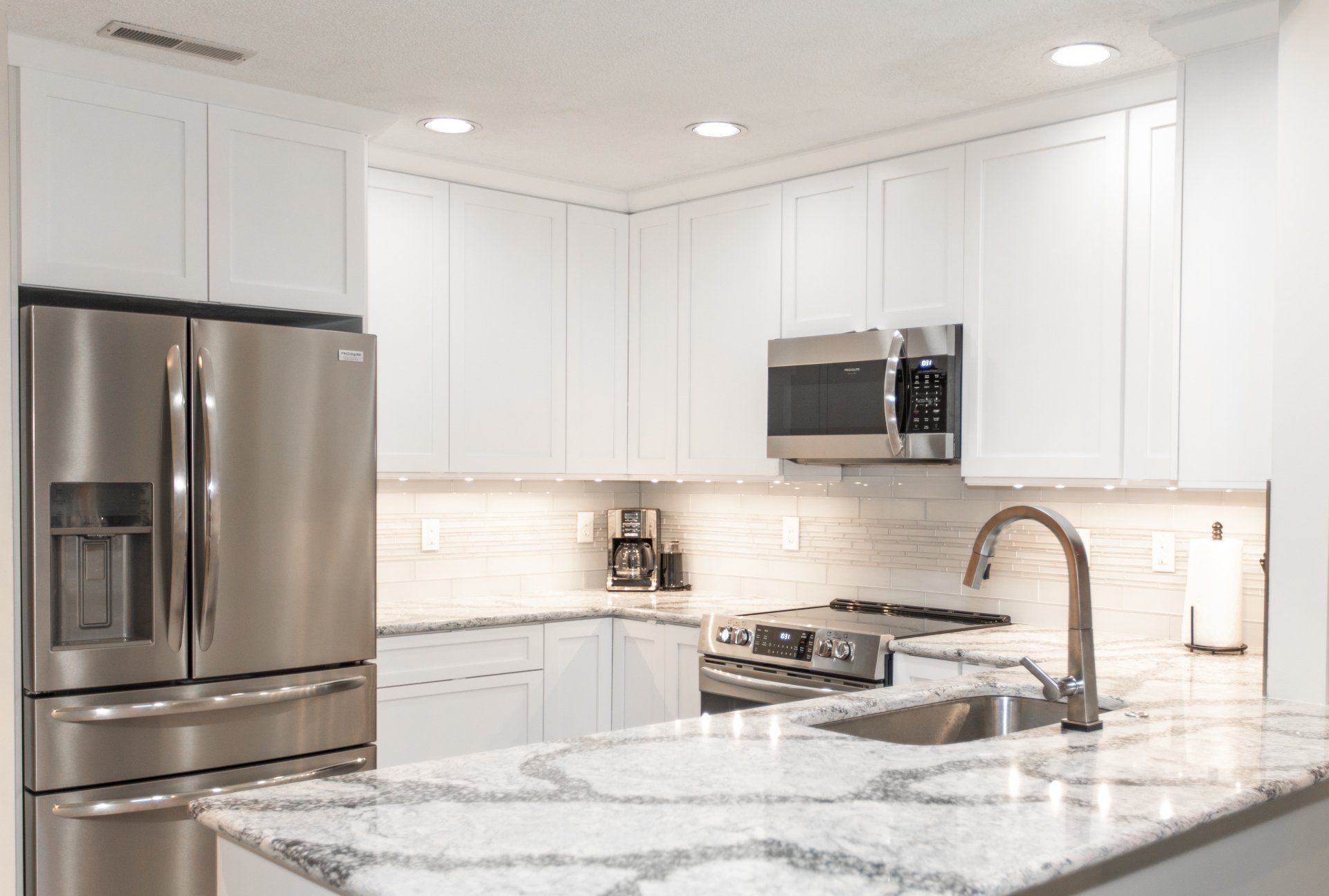 Modern white kitchen with stainless steel appliances, granite countertops, and overhead lighting.