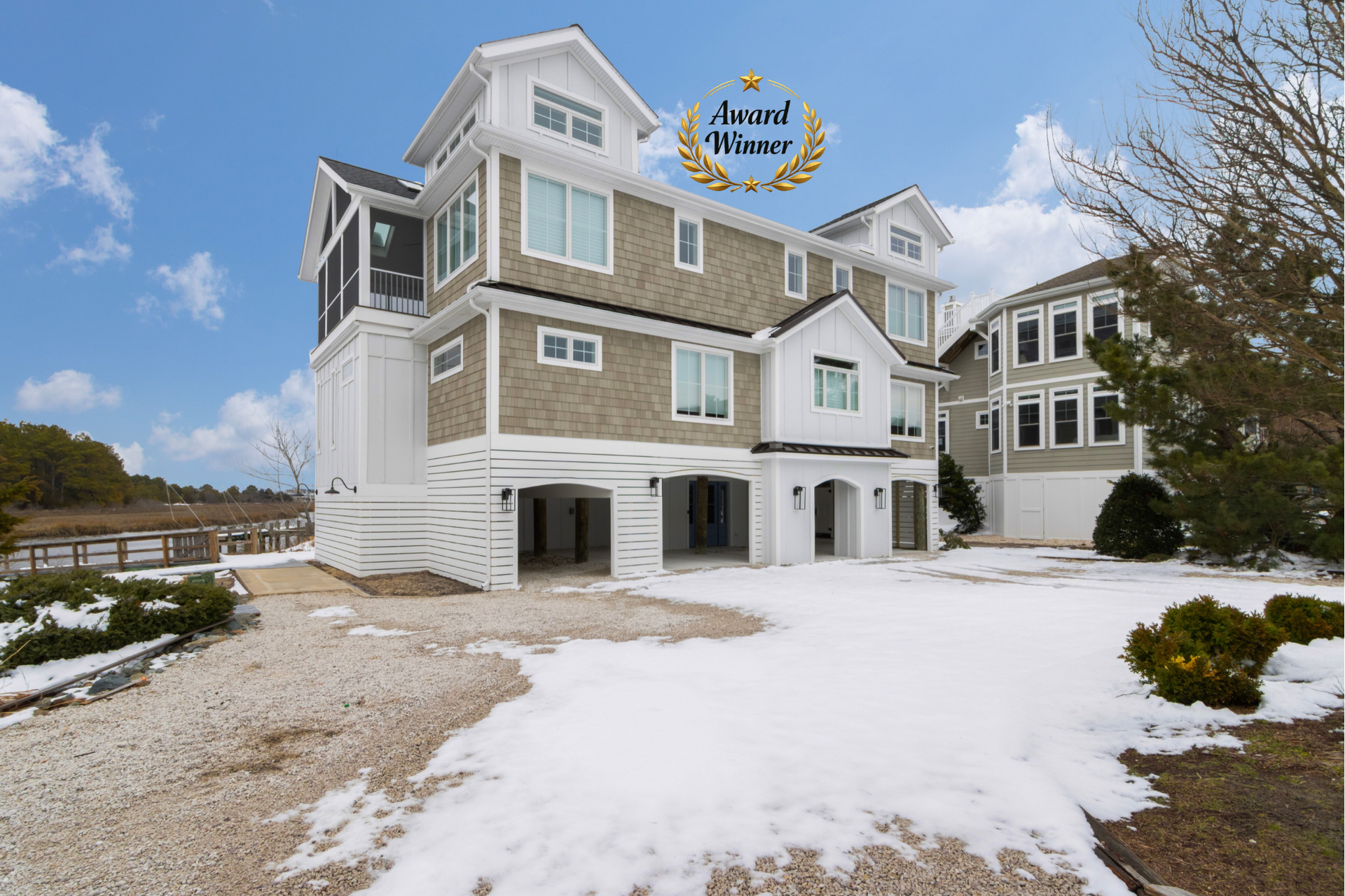 Snow-covered beach house with gray siding and white trim under a blue sky
