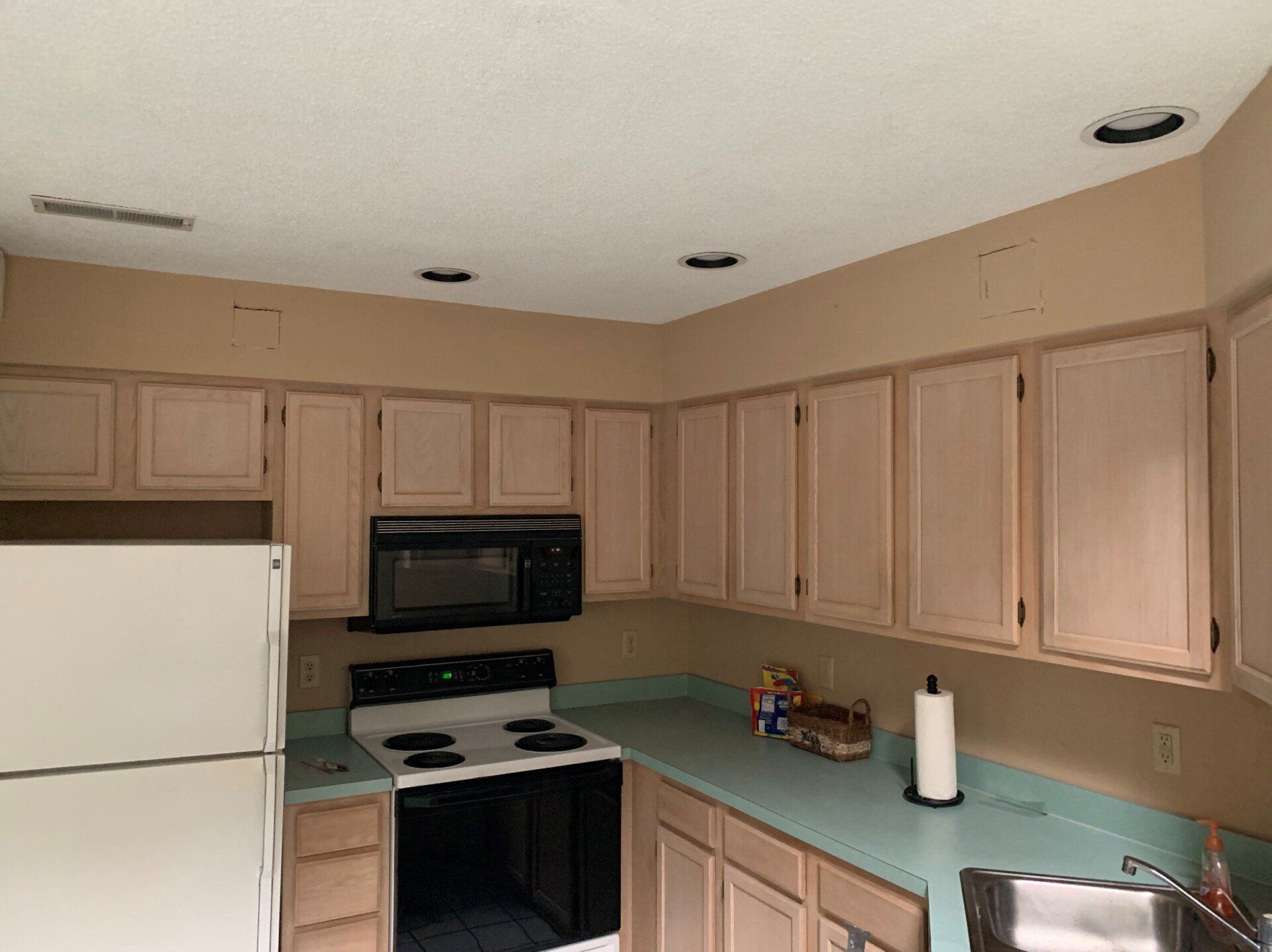 Kitchen with light tan cabinets, black appliances, and a teal countertop.