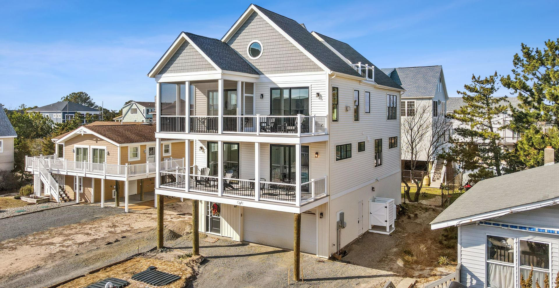 Raised white coastal house under construction with wraparound porches and blue sky.