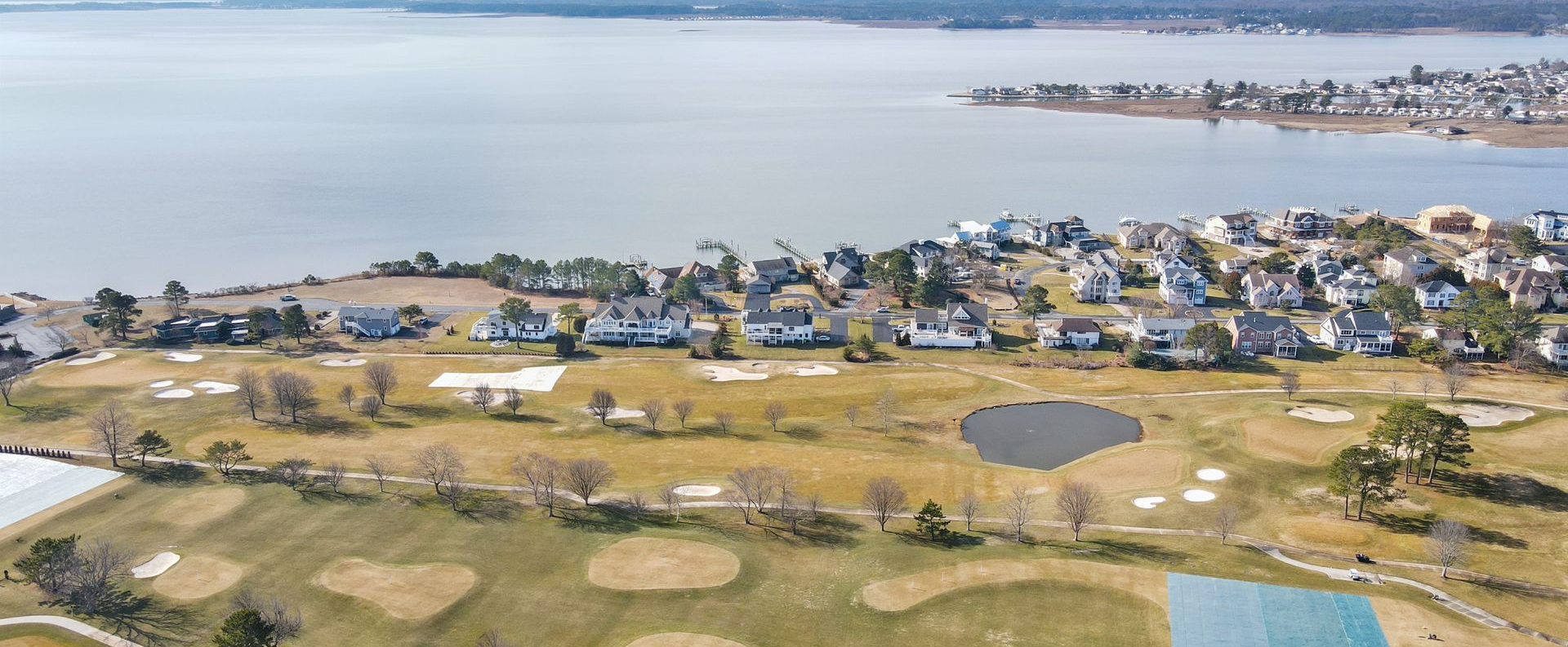 Aerial view of a coastal town, open grassy fields, and a wide bay under a clear blue sky.