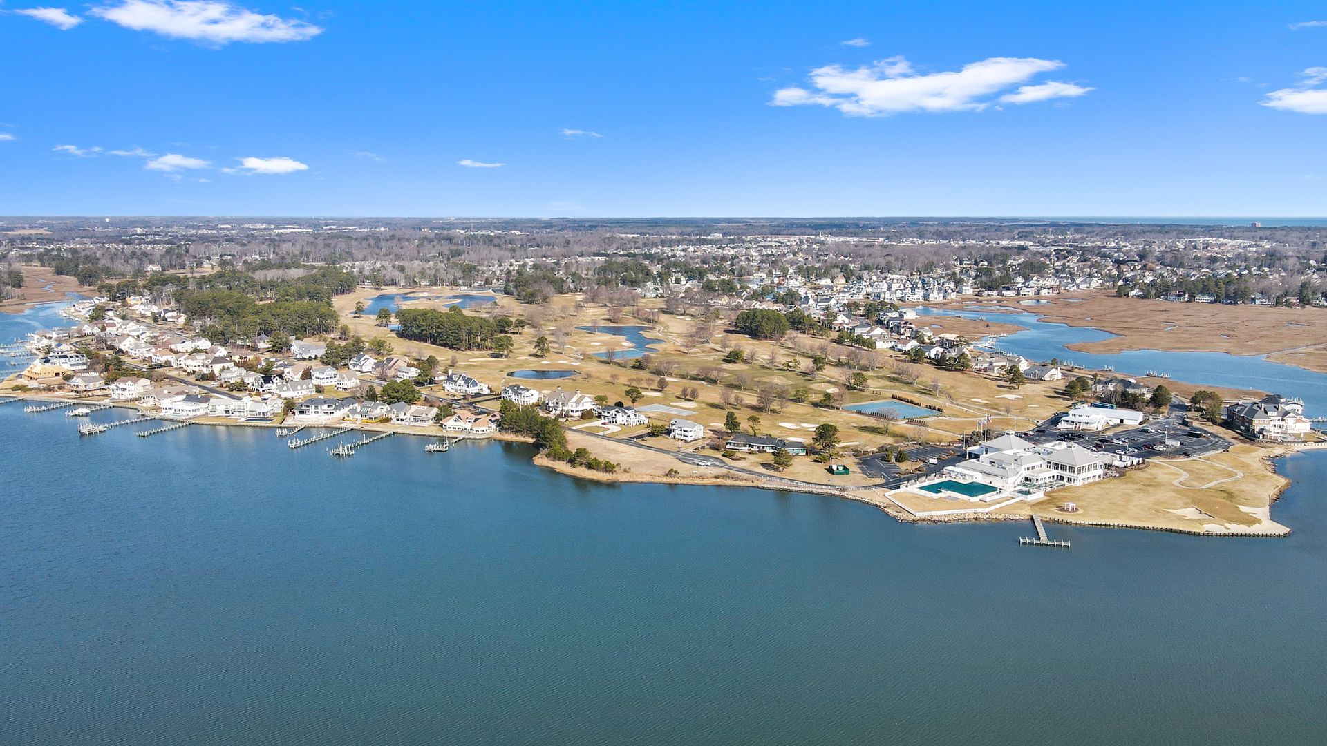 Aerial view of a coastal island with houses, a golf course, and water. Clear blue sky overhead.