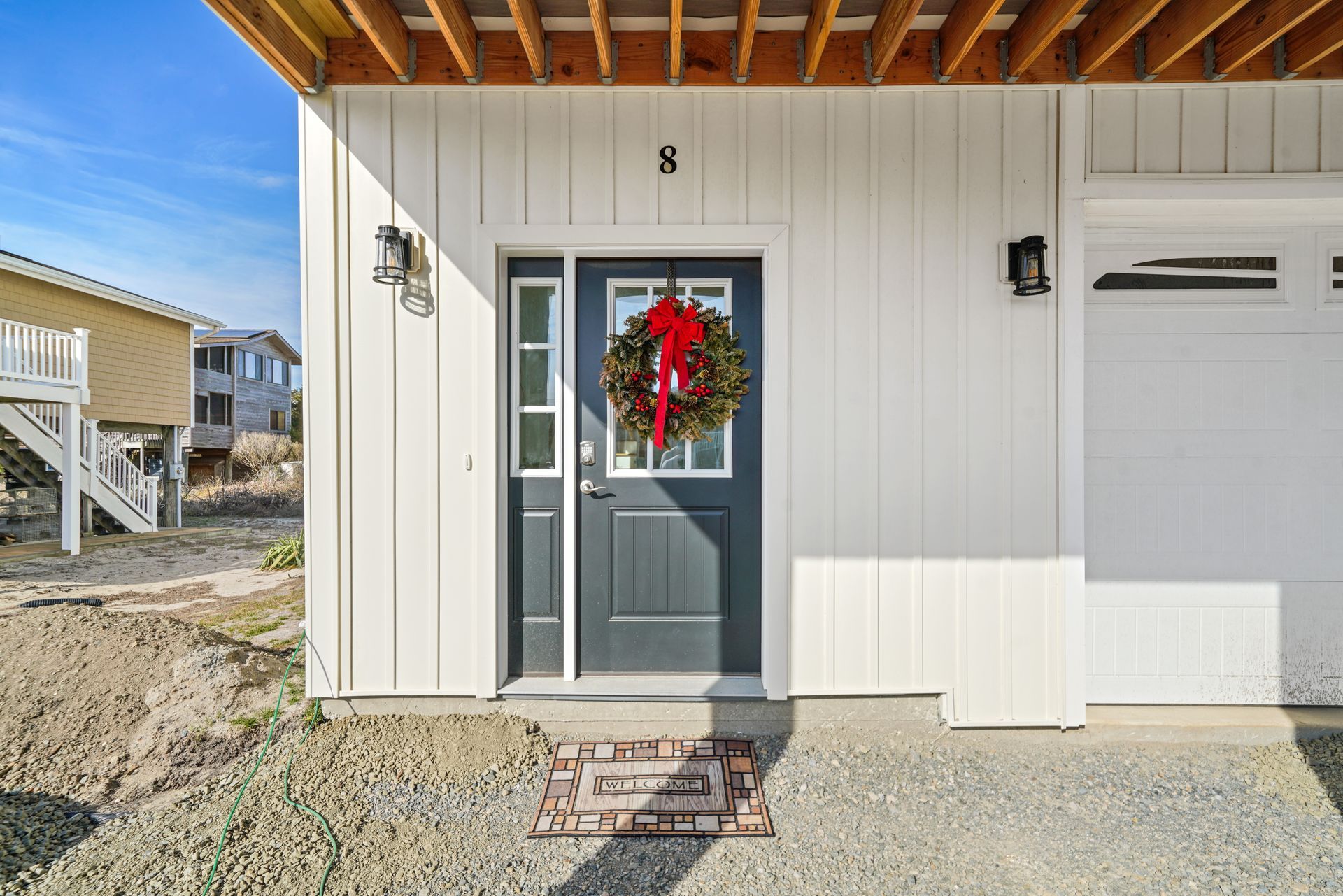 Front entrance of a house with a gray door, red wreath, and small step on a gravel path.