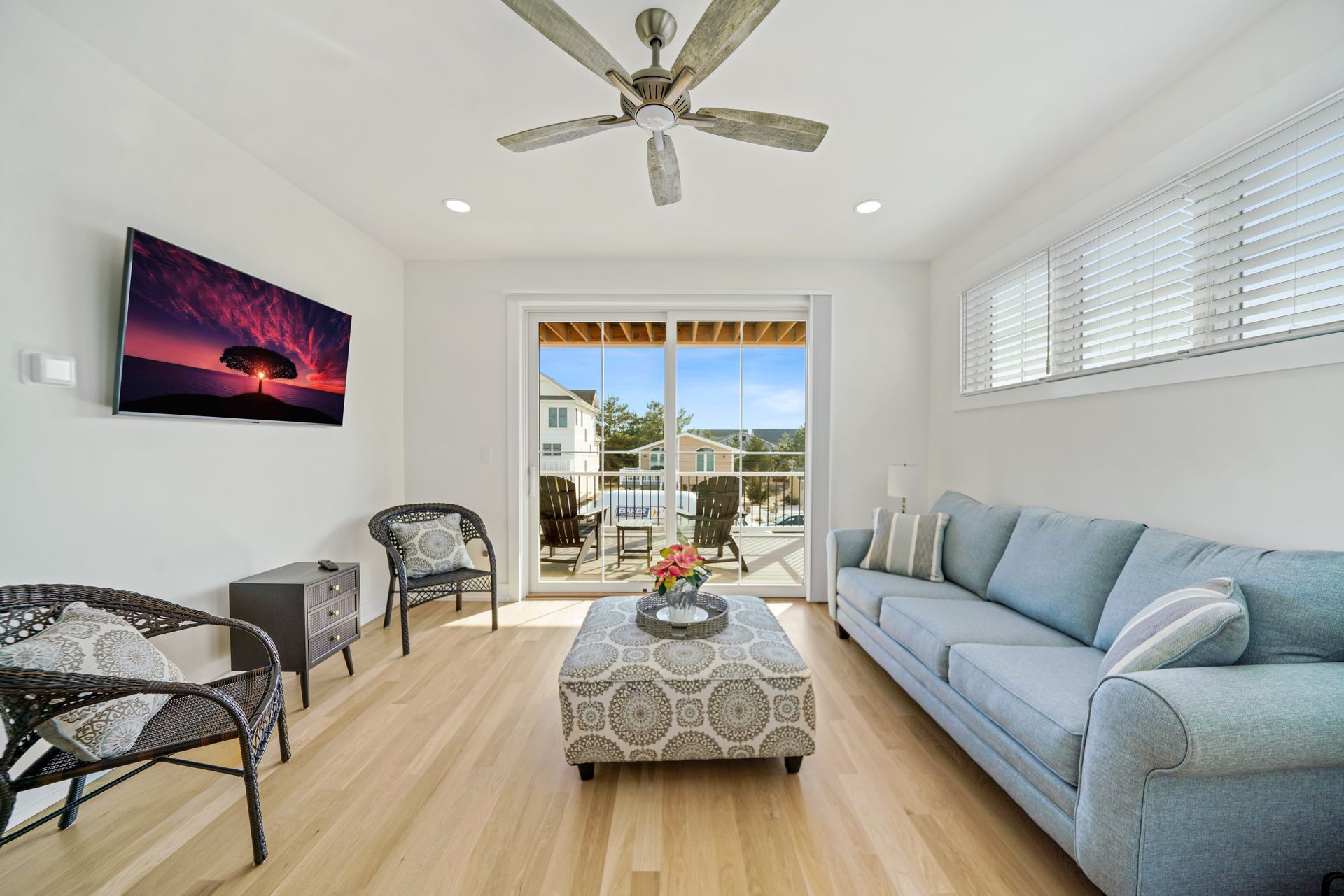 Bright living room with blue sofa, patterned chairs, ceiling fan, and open sliding doors to a patio and ocean view