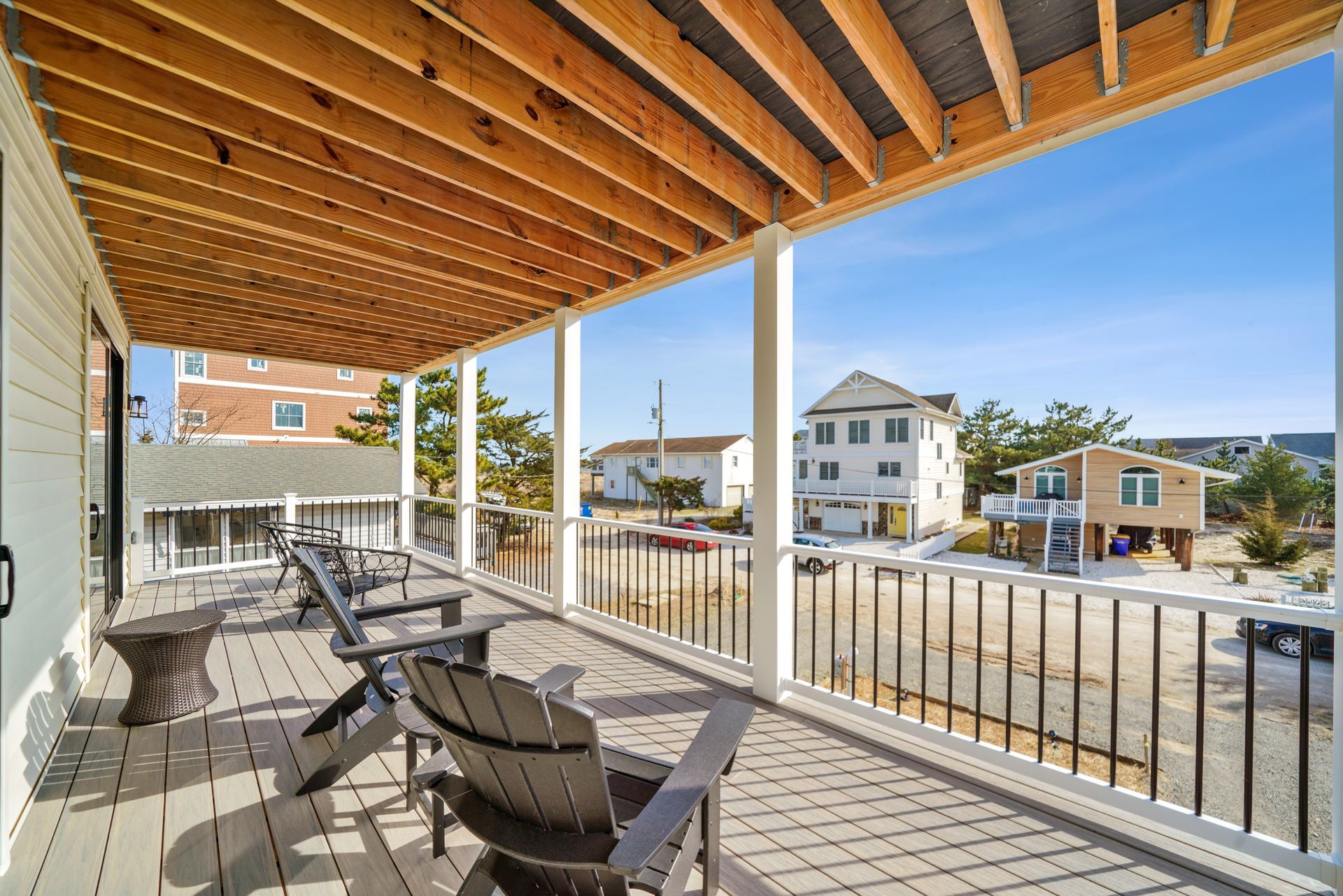 Covered porch with lounge chairs overlooking a sunny residential street and houses