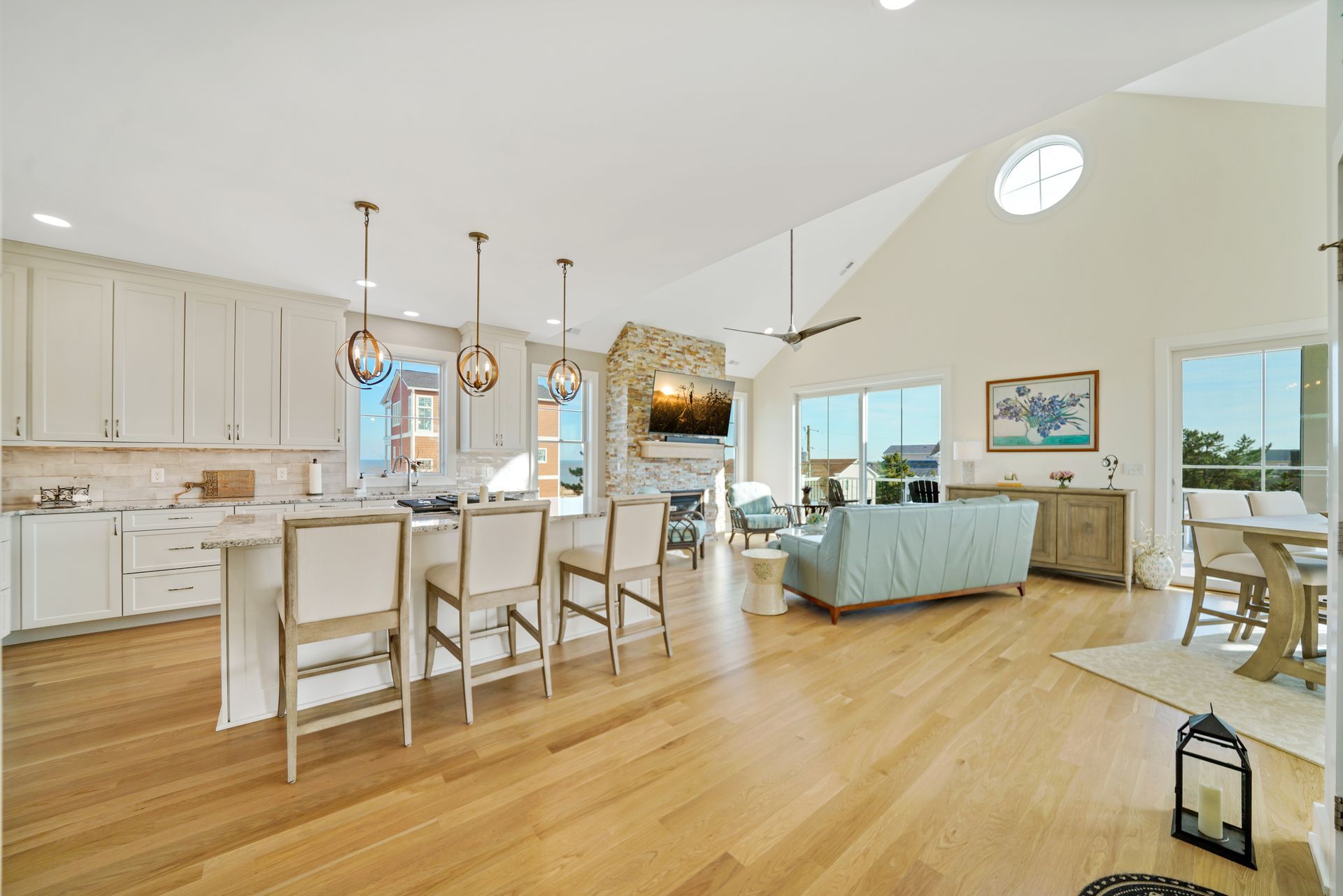 Bright open kitchen and living room with wood floors, white cabinets, blue sofa, and pendant lights