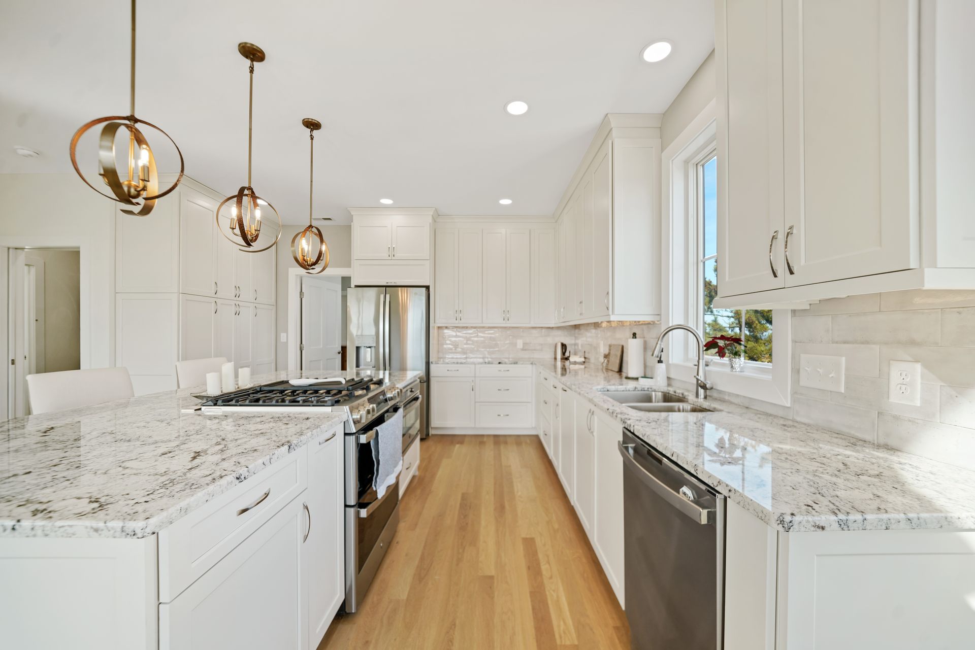 Bright modern kitchen with white cabinets, marble counters, brass pendant lights, and stainless steel appliances