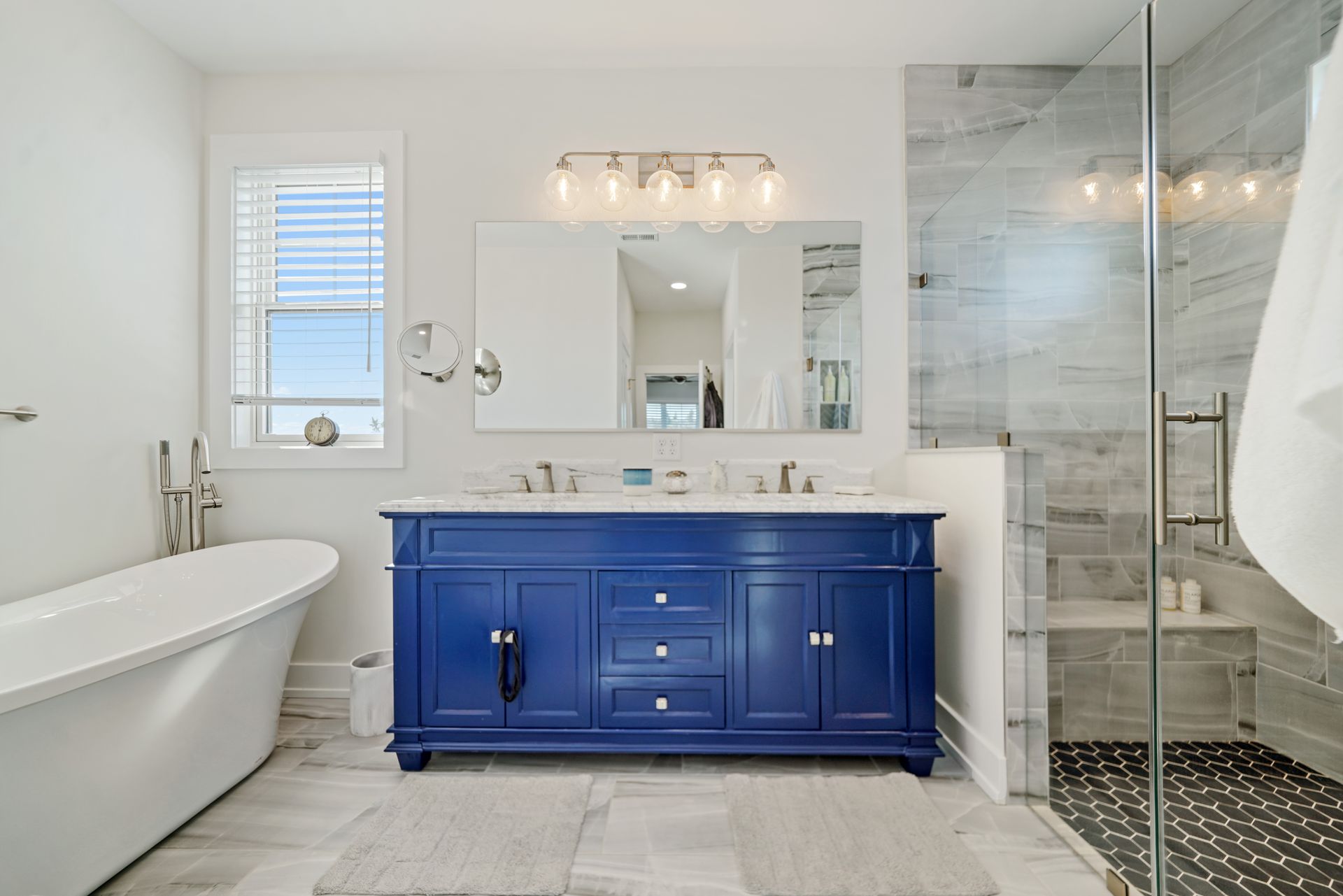 Modern bathroom with blue vanity, freestanding tub, and glass shower
