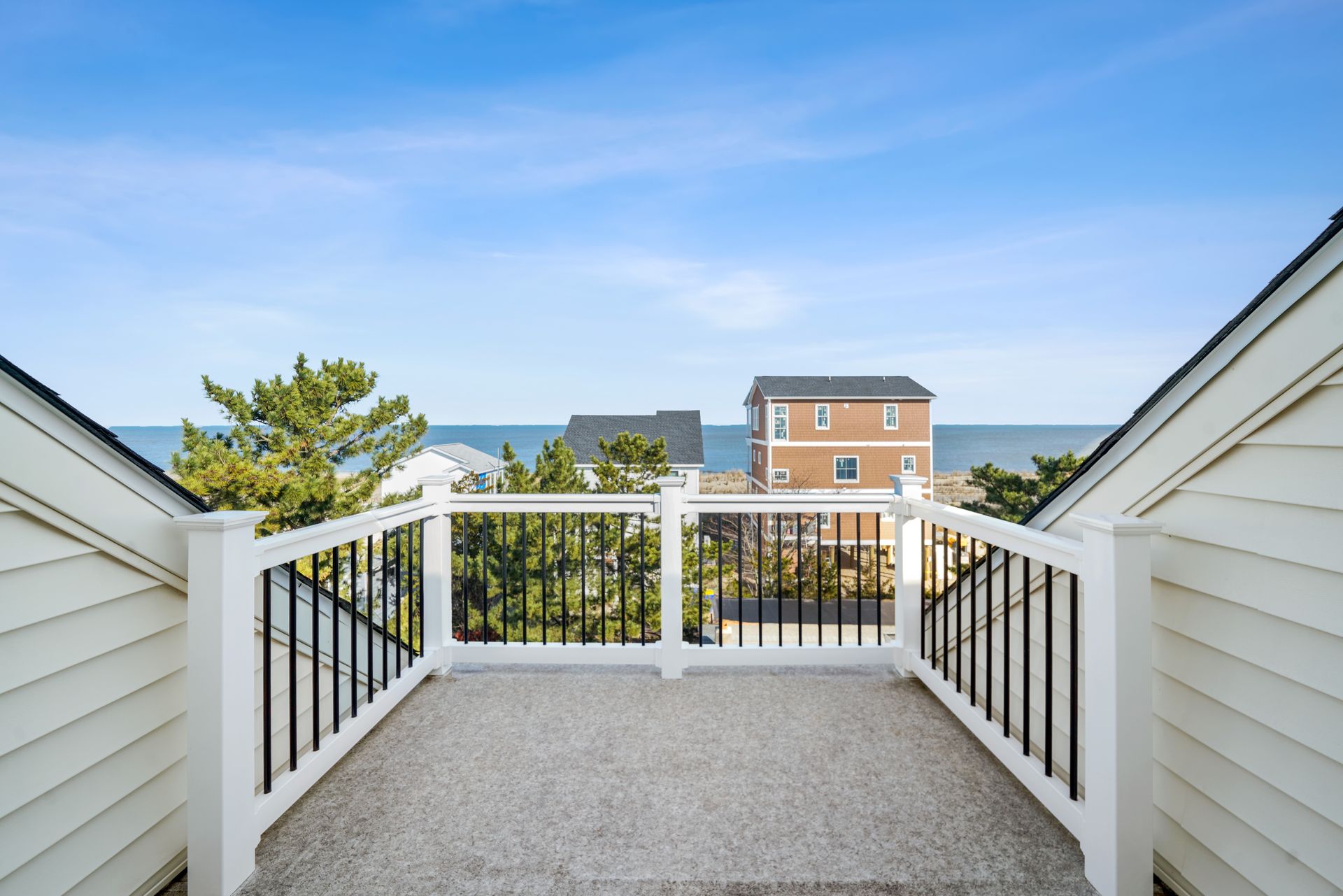 Balcony view of oceanfront homes and blue sky beyond white railings