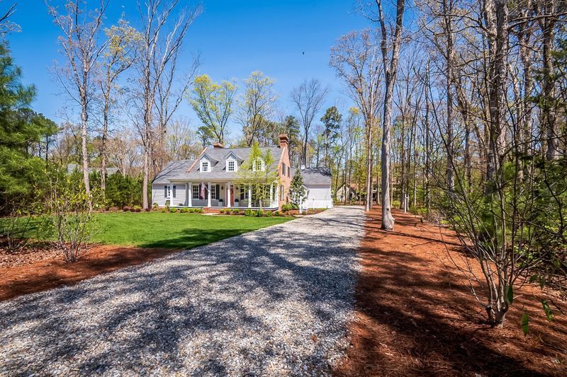 Curb appeal home with a gravel driveway, porch, and a surrounding forest on a sunny day.