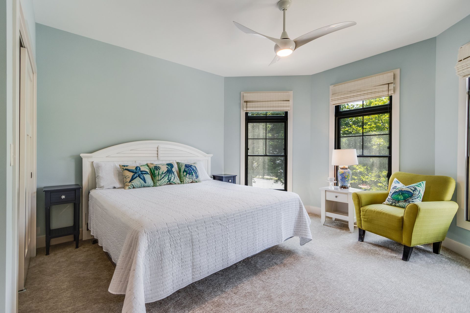 Bedroom with a light blue wall, white bed, green armchair, and a window with a view.