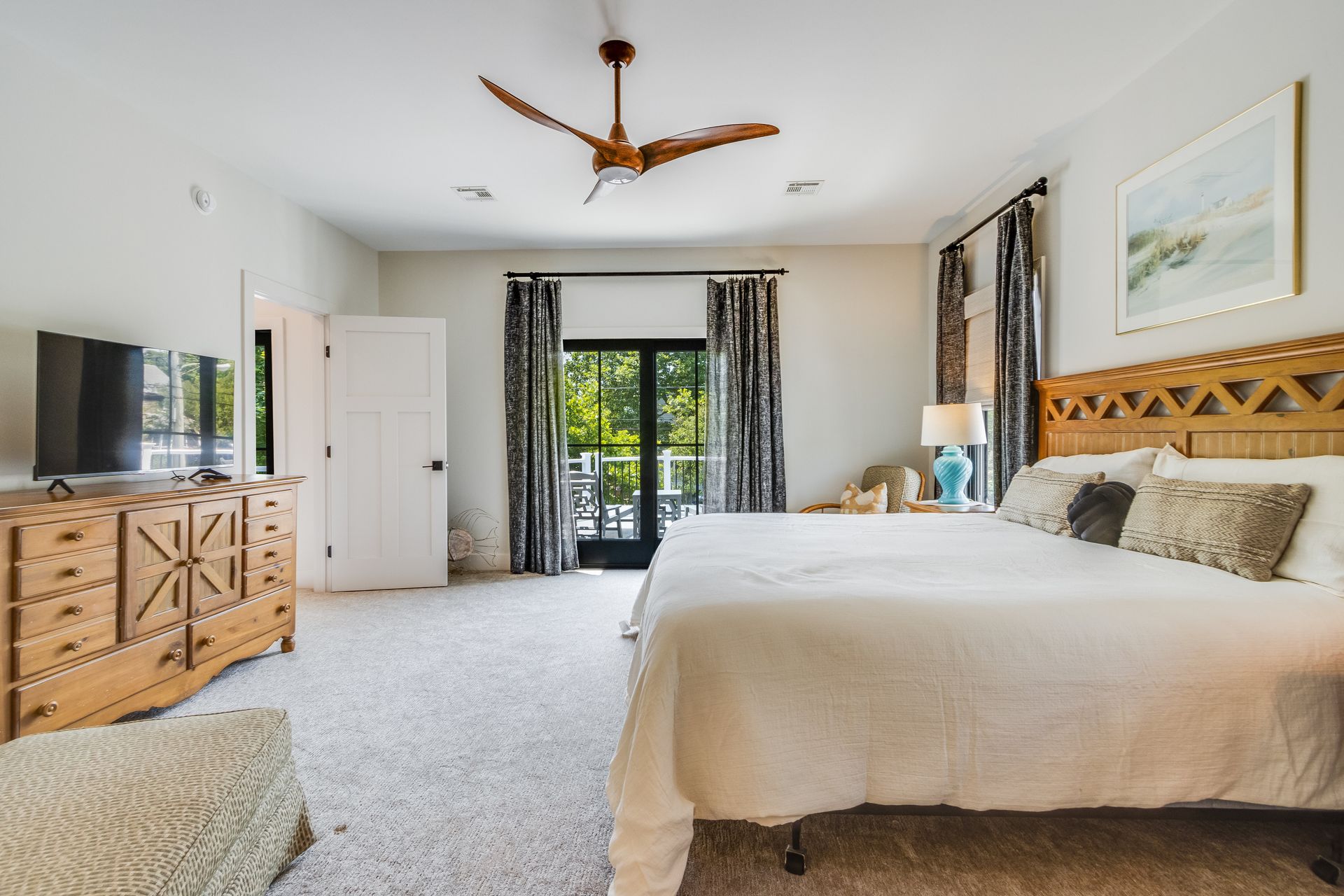 Bedroom with a king bed, dresser, door to a balcony, ceiling fan, and light-colored carpet.