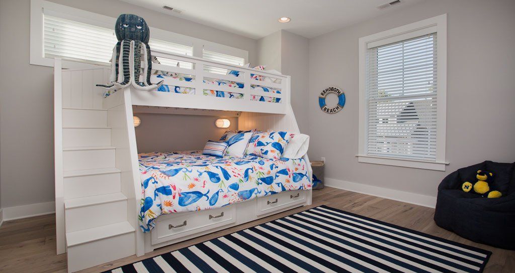 White bunk bed in a coastal-themed room with ocean-patterned bedding, a striped rug, and bean bag chair.