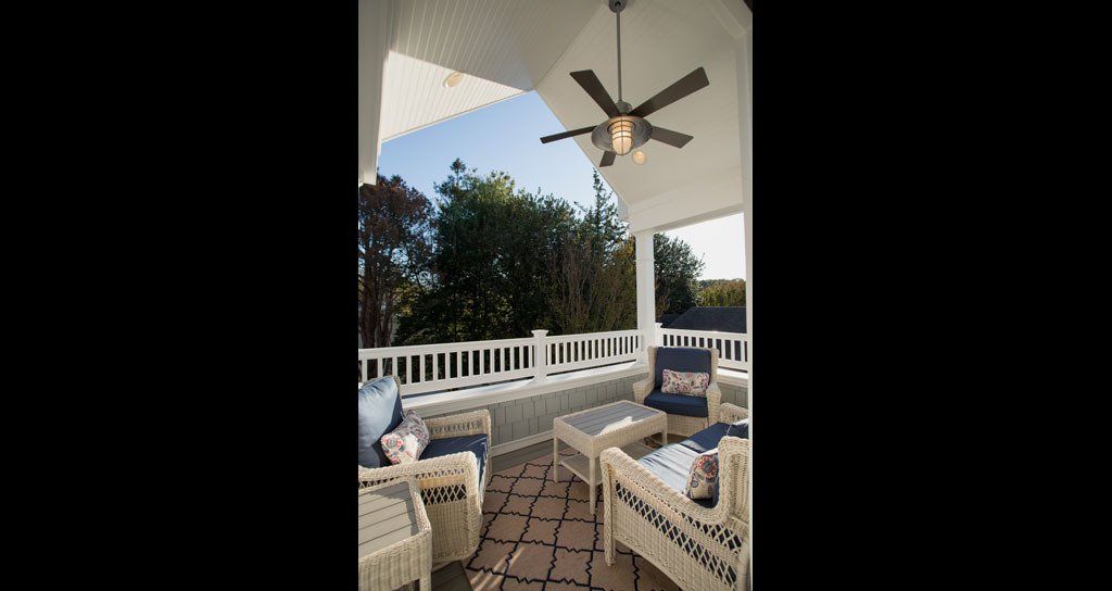Covered porch with white railings, wicker furniture, and a ceiling fan.