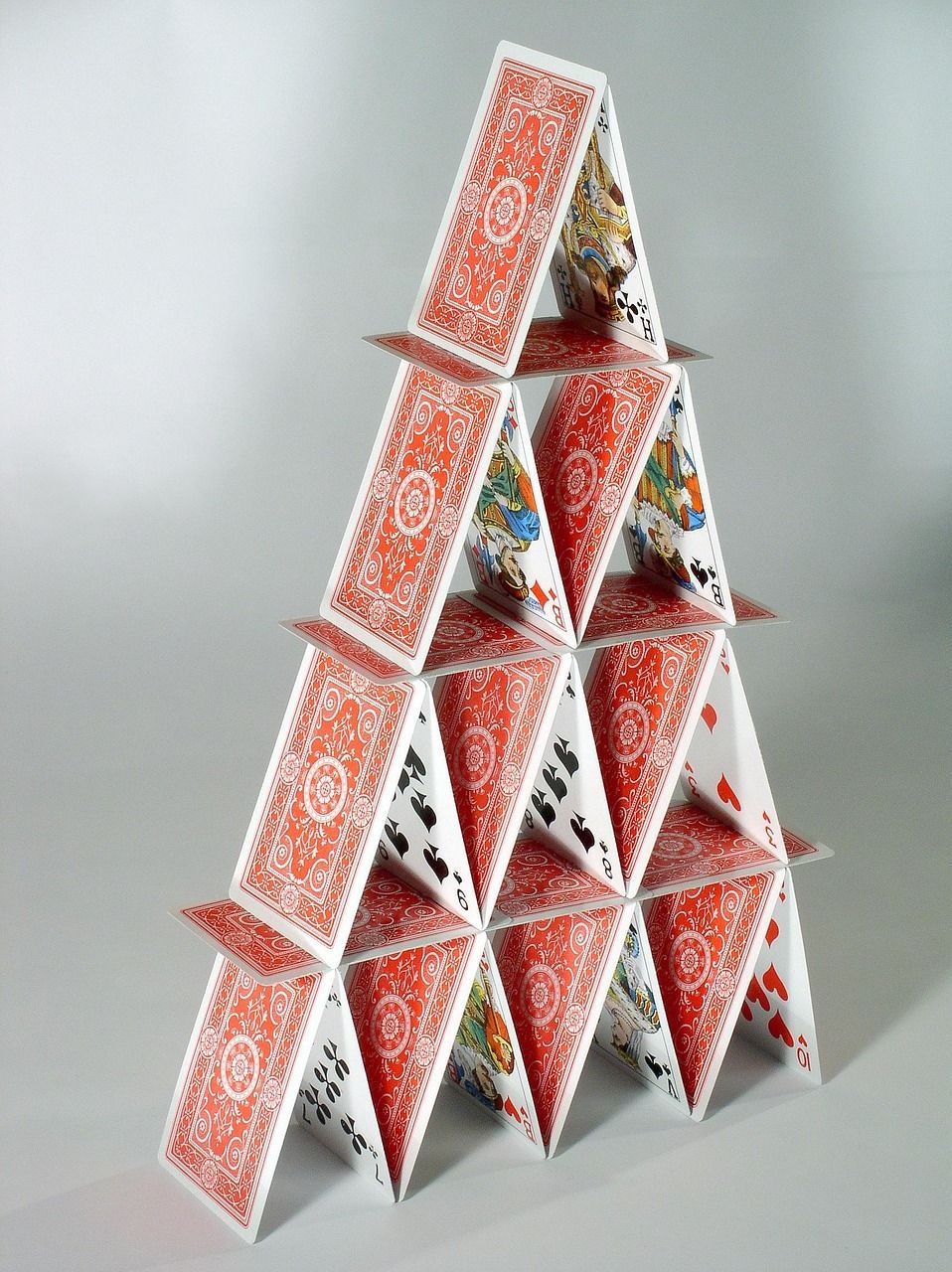 A house of cards, red and white playing cards arranged in a triangular structure on a gray surface.
