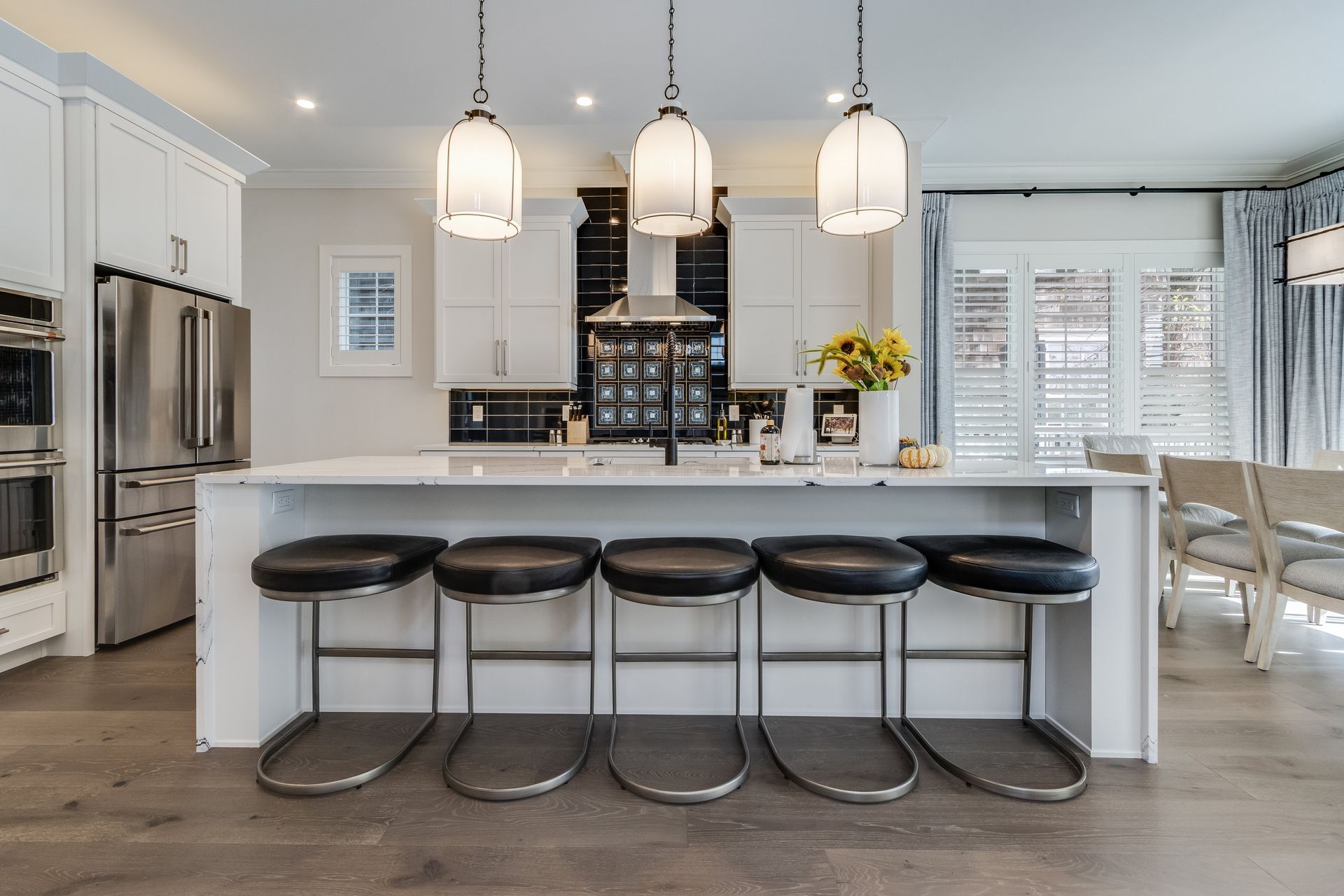 Modern kitchen with white cabinets, stainless steel appliances, island with stools, and pendant lights.