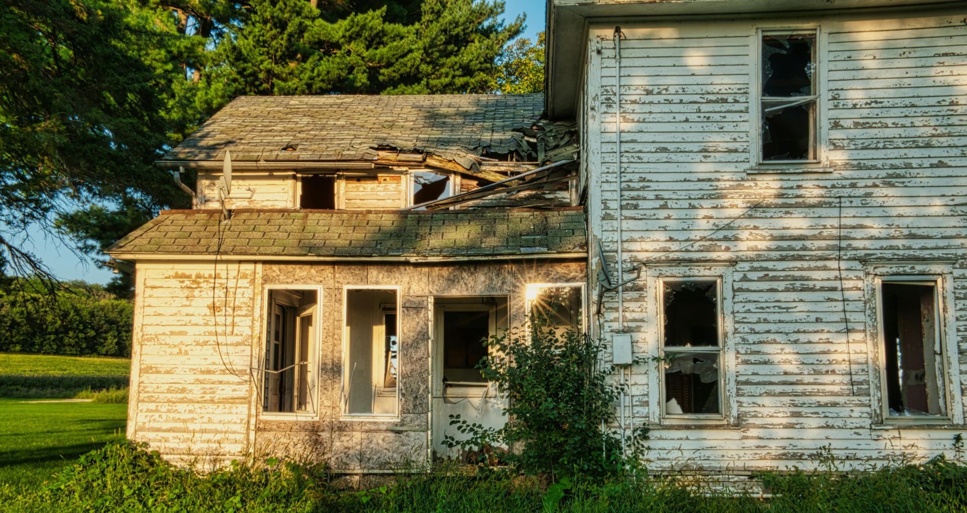 Abandoned weathered house with peeling paint and overgrown grass in a sunny rural field