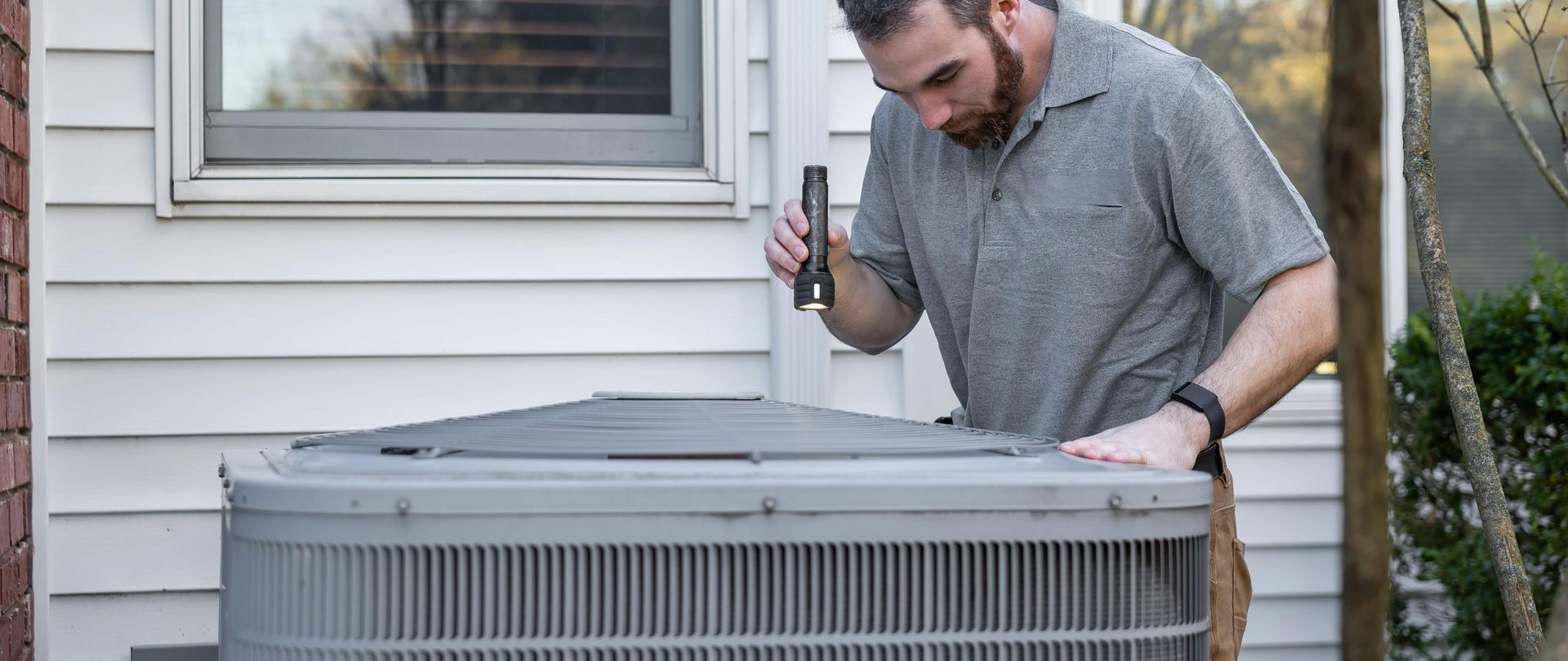 Man inspecting a large outdoor air conditioner unit beside a house