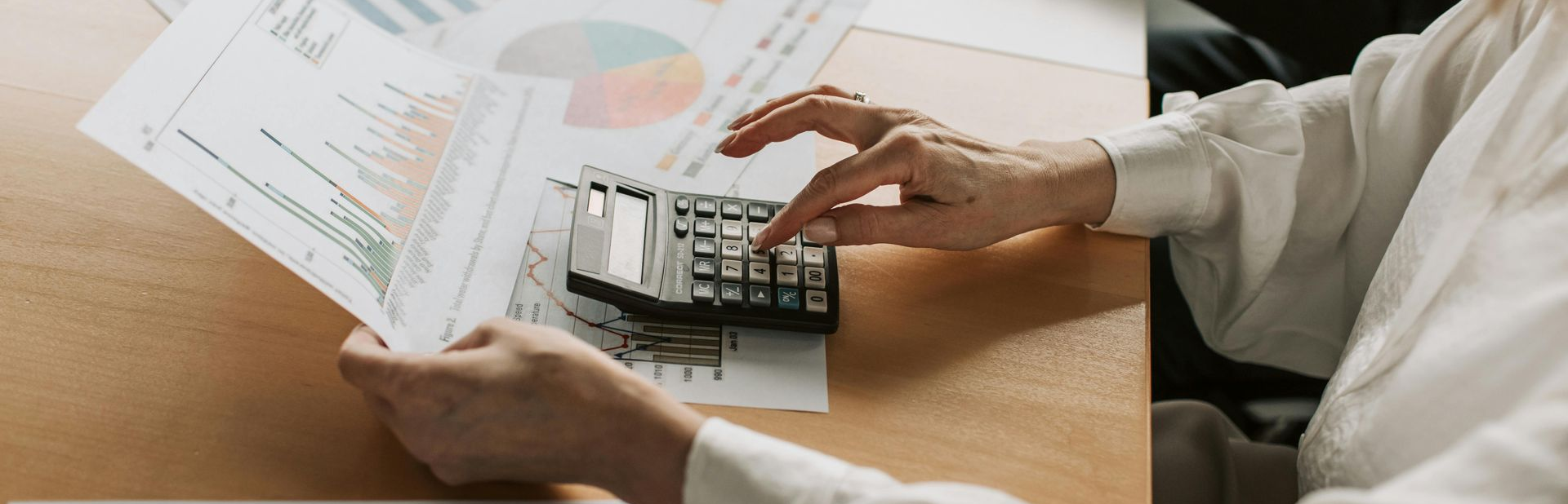 Hands using a calculator beside financial charts and papers on a desk
