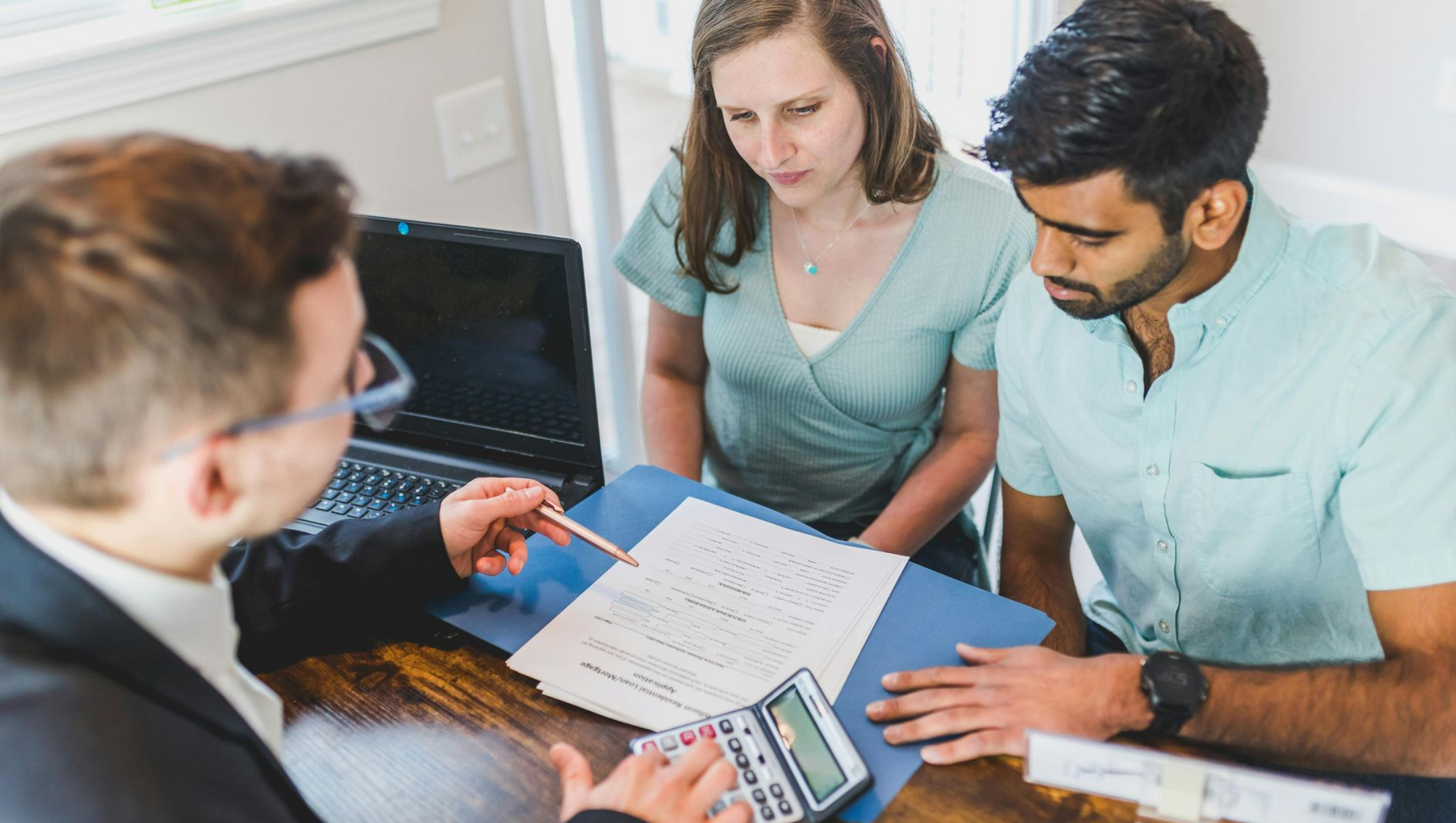 Three people reviewing paperwork and a calculator at a table in an office meeting