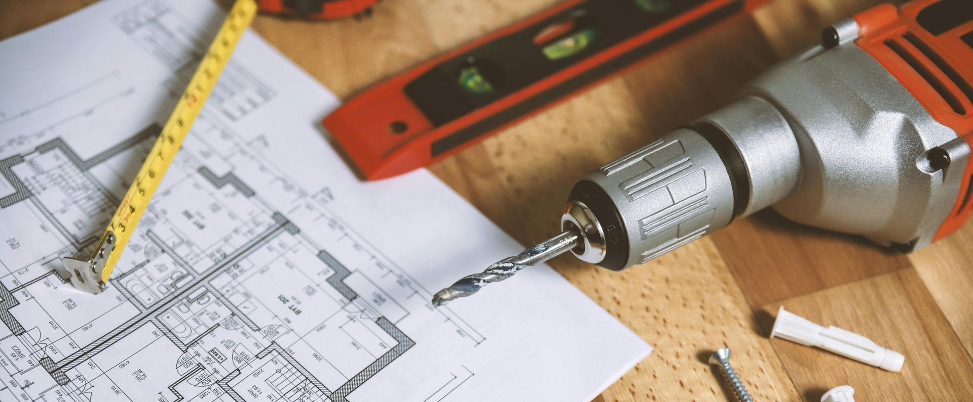 Construction tools: blueprint, drill, level, and tape measure on a wooden surface.